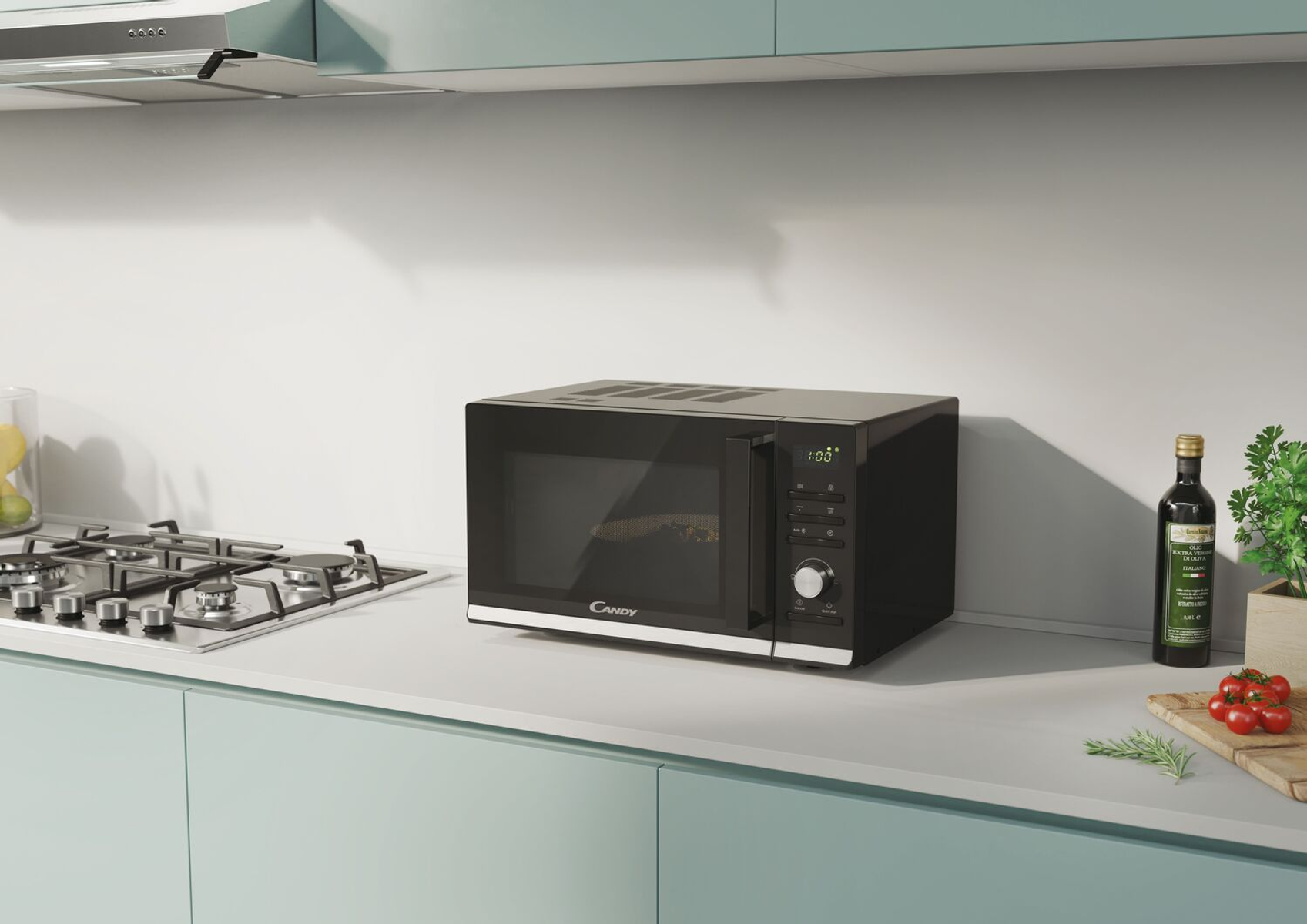 Czarna kuchenka mikrofalowa na blacie w kuchni. Kuchenka gazowa po lewej. Widoczna oliwa z oliwek i pomidory.
