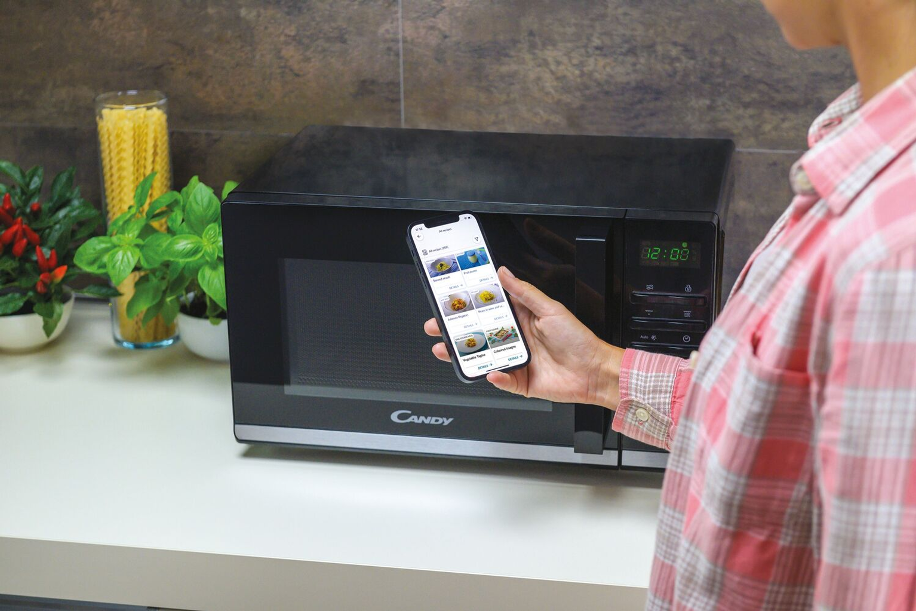 Kobieta używa smartfona przed czarną kuchenką mikrofalową, w otoczeniu kuchni.