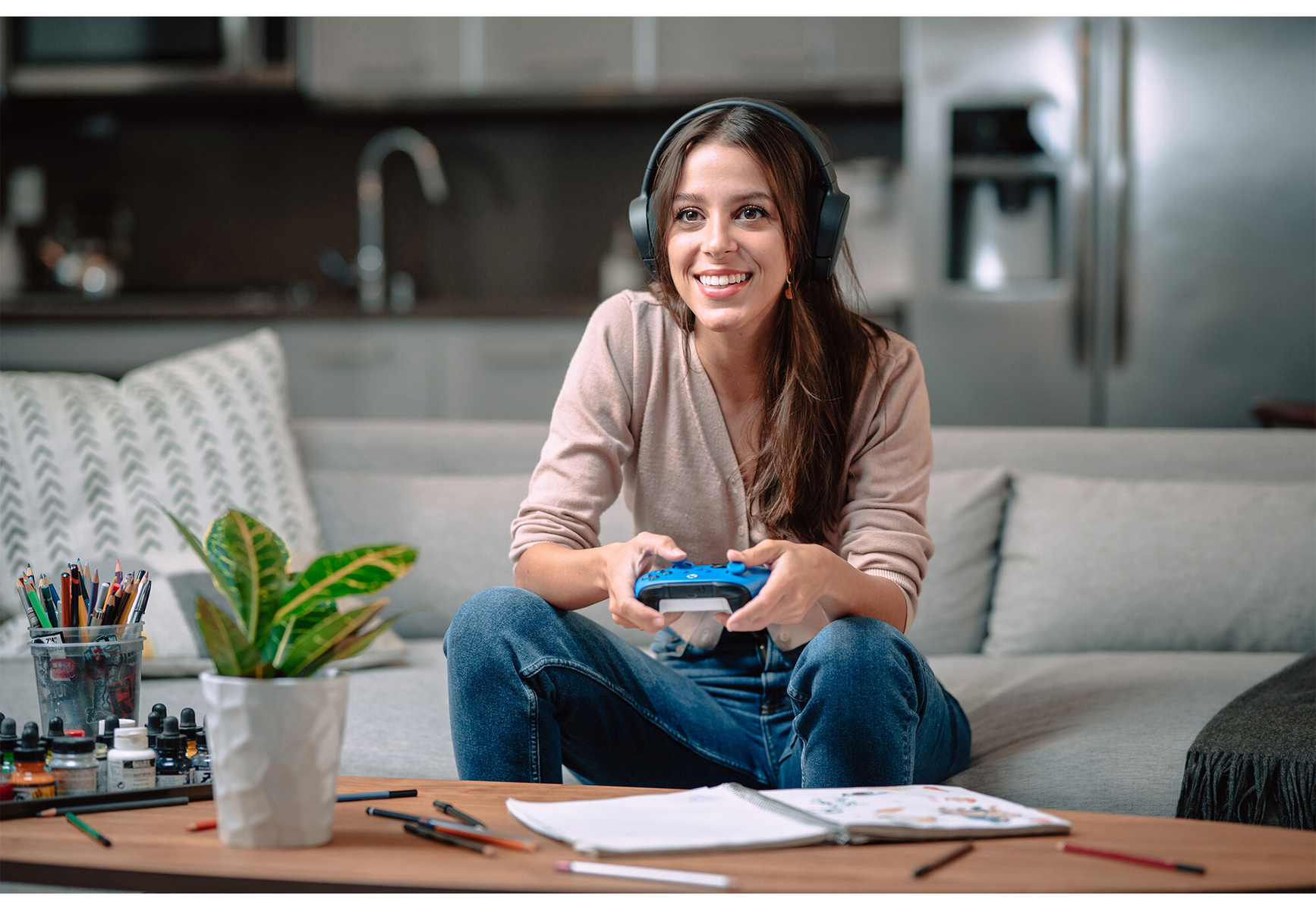 Eine Frau mit Kopfhörern und einem blauen Gamecontroller. Sie sitzt auf einem Sofa.