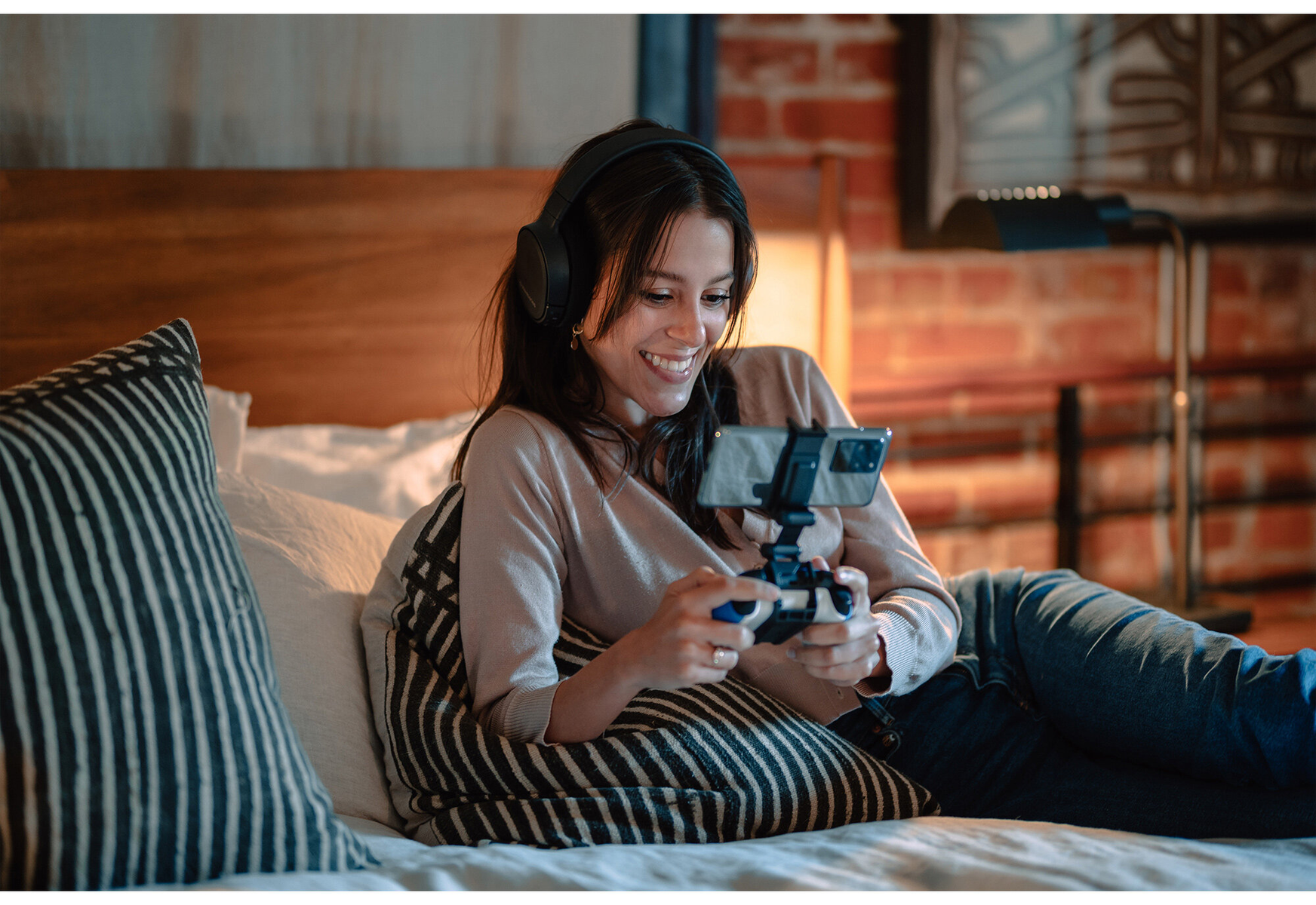 Frau im Bett spielt ein Spiel auf ihrem Handy mit Kopfhörern. Sie lächelt und genießt das Spiel.