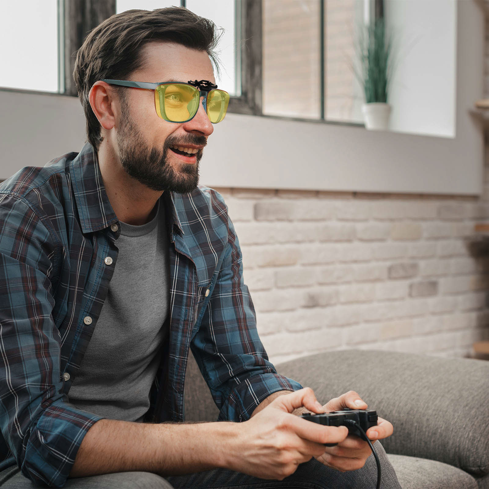 Ein Mann mit gelb getönten Brillen spielt ein Videospiel mit einem Controller in häuslicher Umgebung.