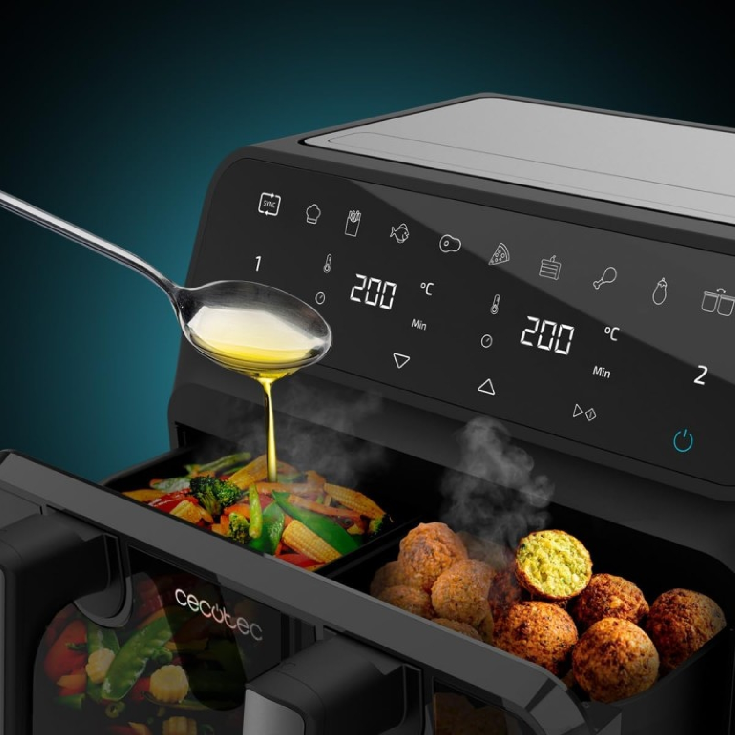 Airfryer met eten erin, lepel giet olie. Groenten en gehaktballen zichtbaar. Donkerblauwe achtergrond.