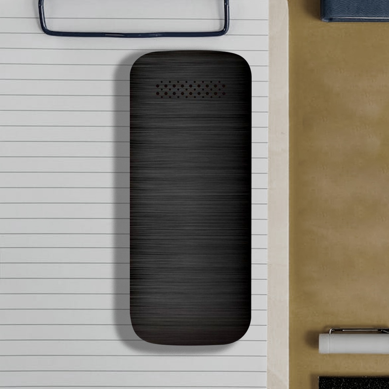 Czarne urządzenie na białej kartce papieru. Urządzenie ma teksturowaną powierzchnię. Otaczają je inne przedmioty.