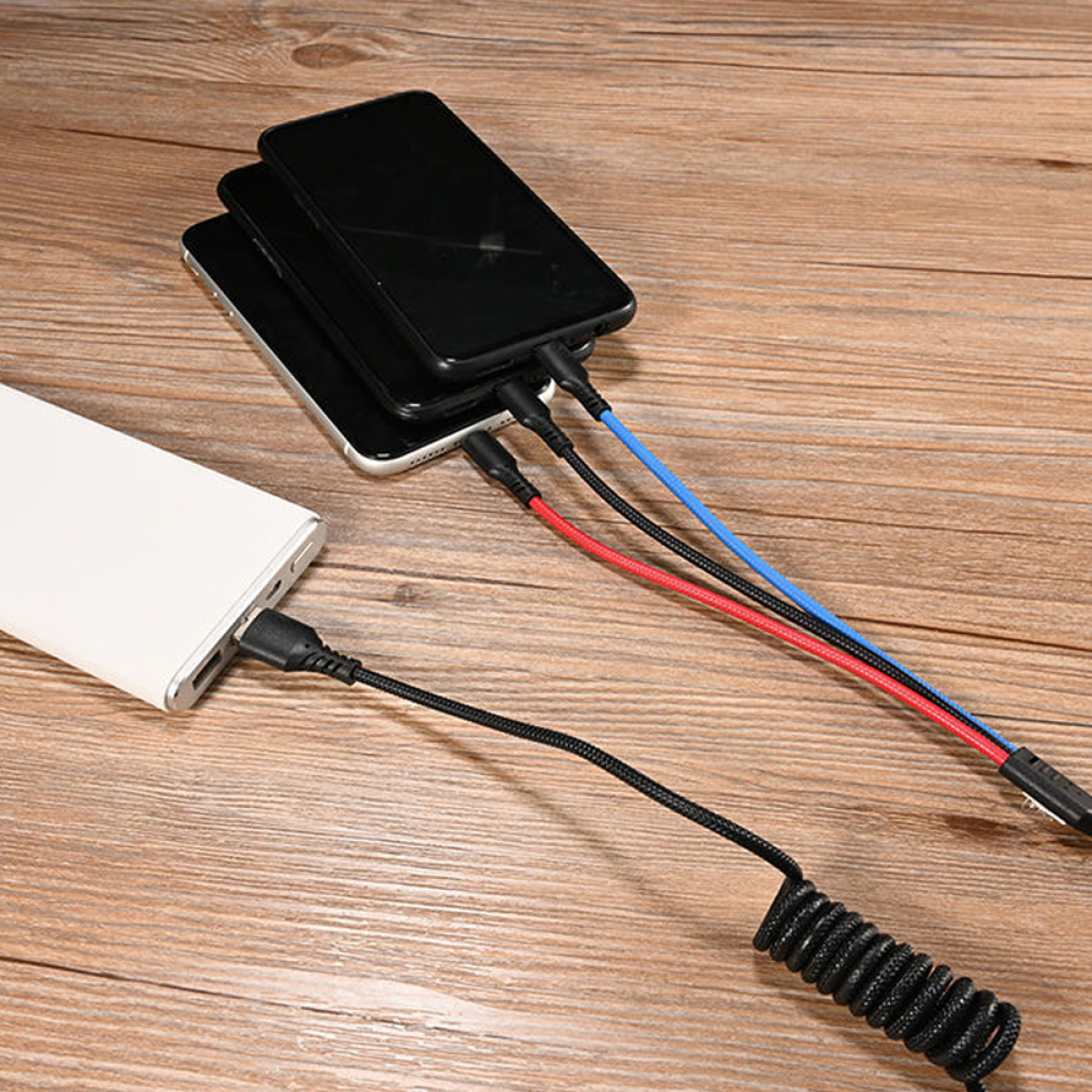 Mehrere Telefone werden mit verschiedenfarbigen Kabeln und einer weißen Powerbank auf einem Holztisch aufgeladen.