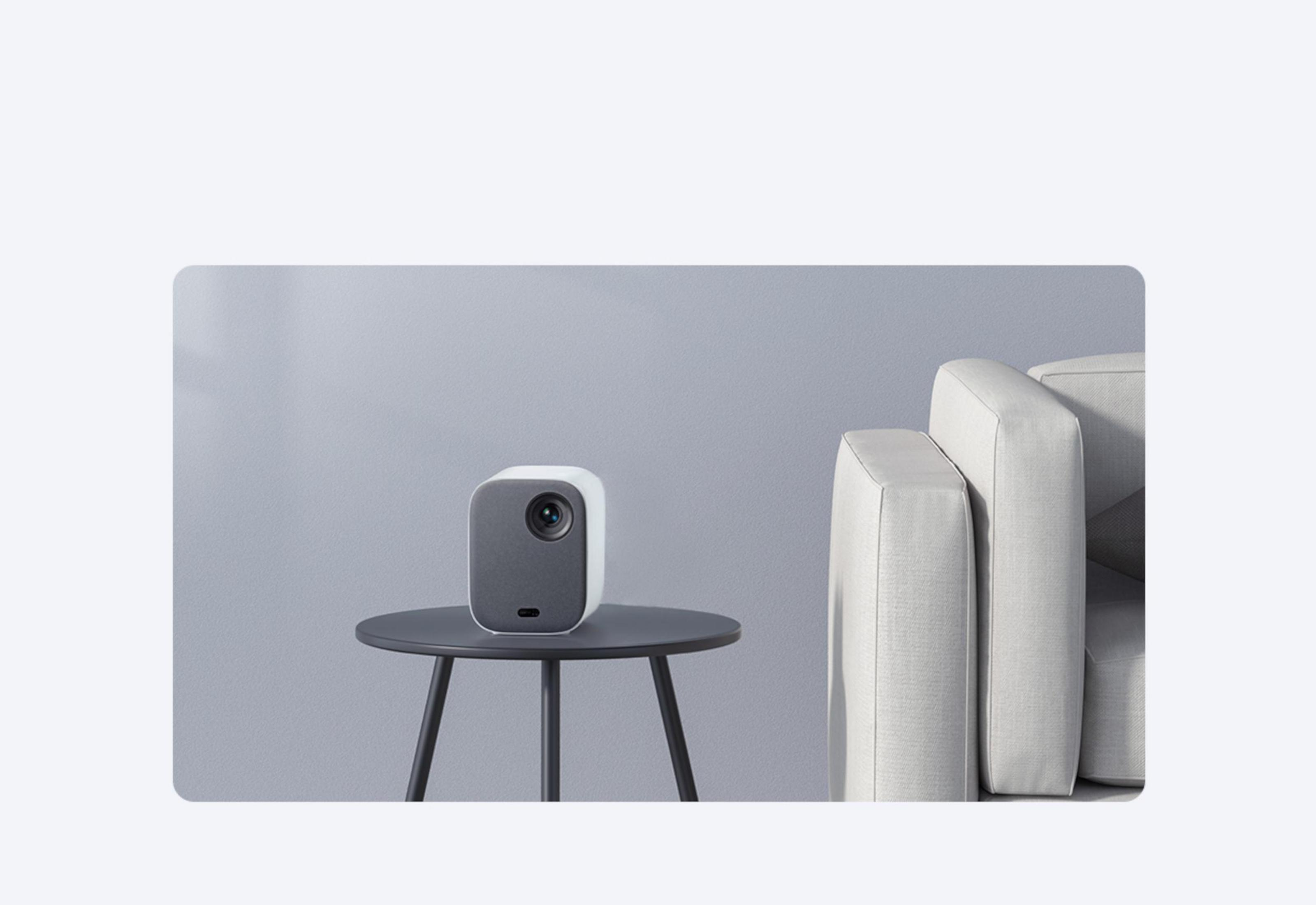 Biały projektor na stole, z kanapą i szarą ścianą w tle.