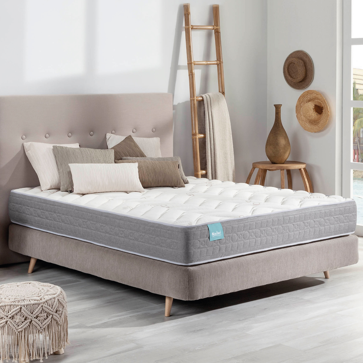 Un colchón en un marco de cama con almohadas, sombreros y una escalera en una habitación bien iluminada.