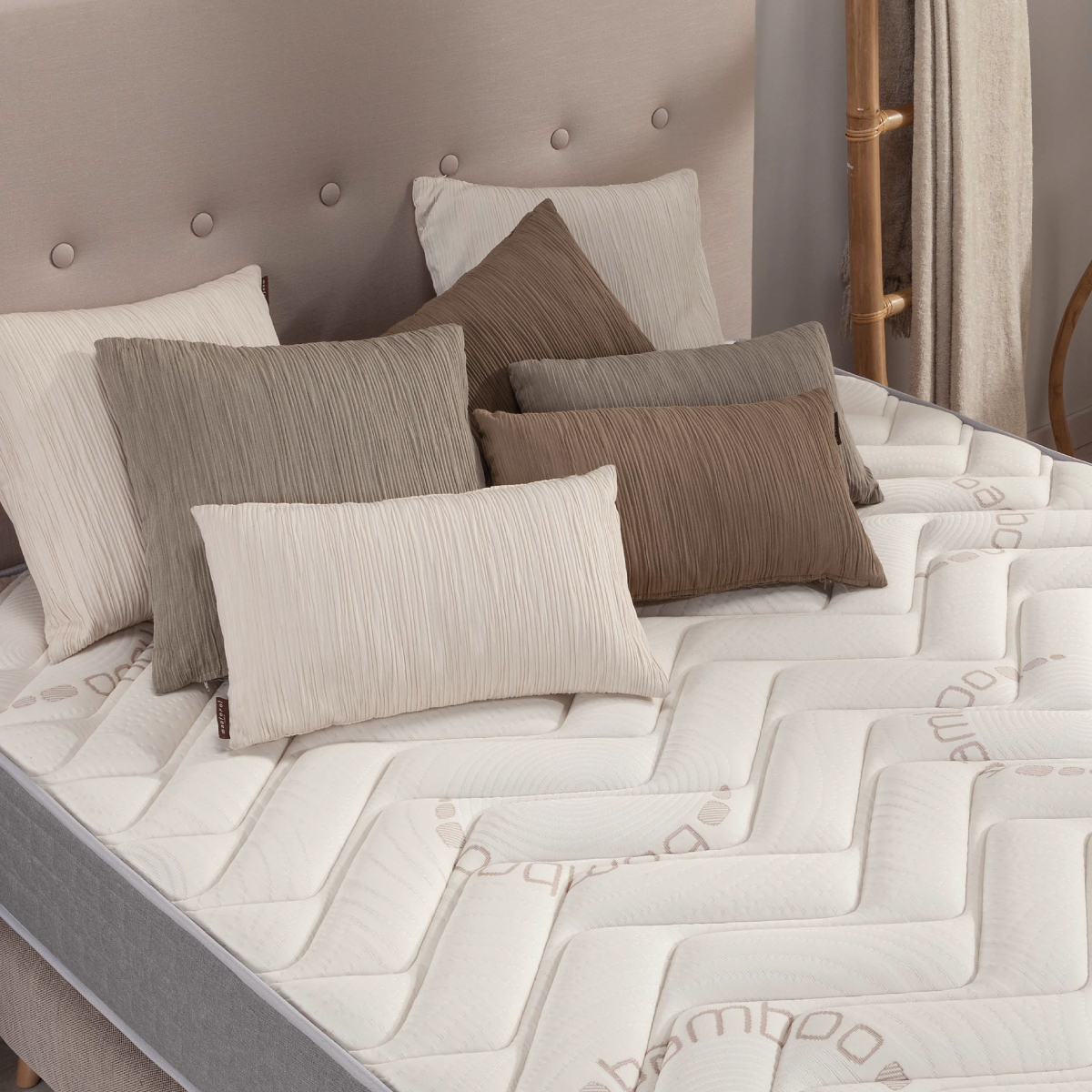 Cama con colchón blanco y gris, con almohadas blancas, grises y marrones.