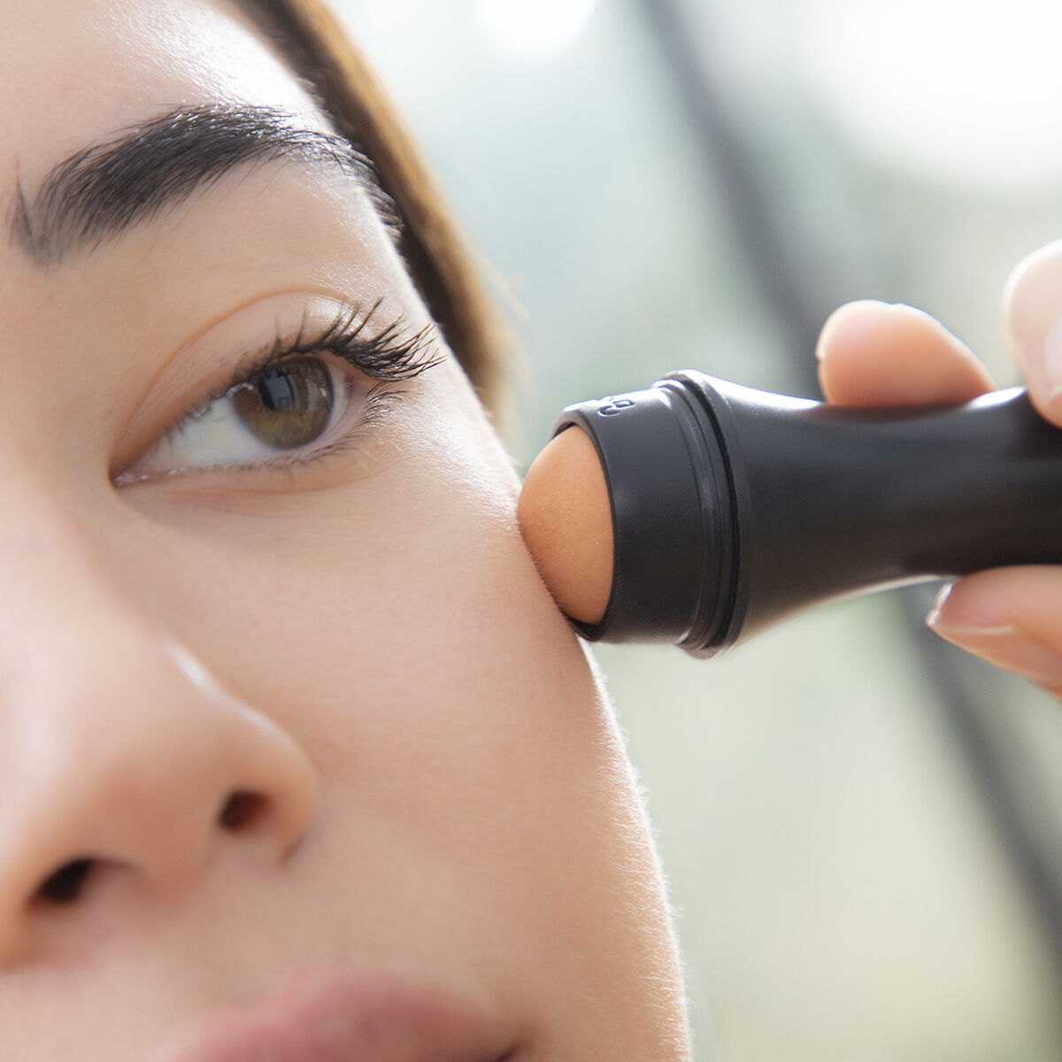 Il viso di una donna con un rullo per trucco nero utilizzato sulla guancia.