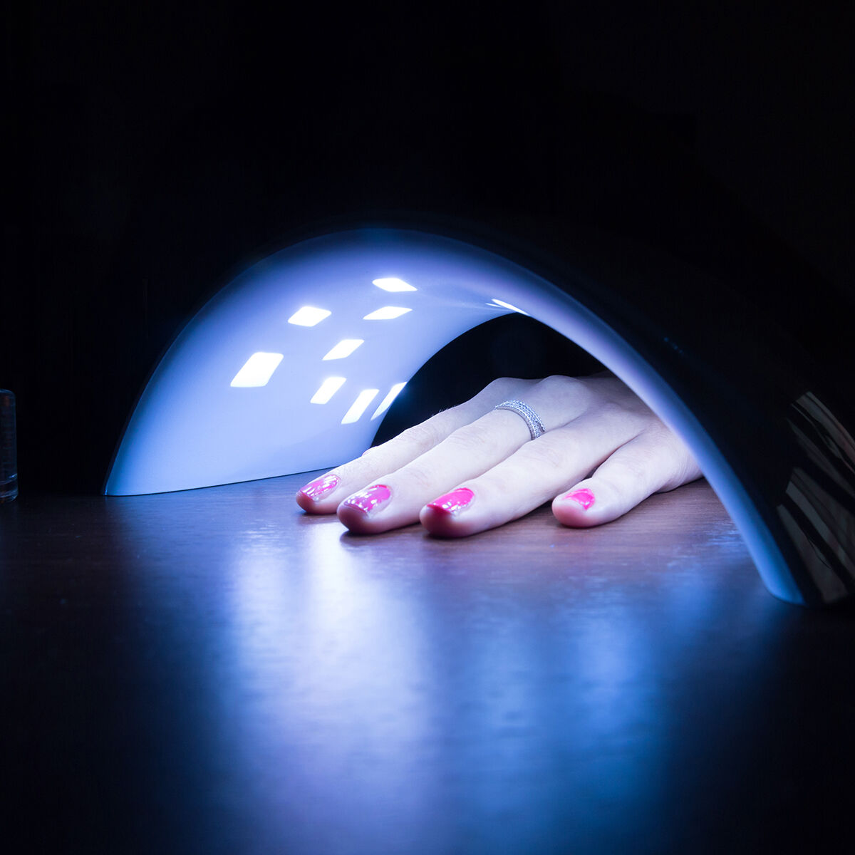 Una mano con uñas rosas en un secador de uñas. La luz azul está brillando.