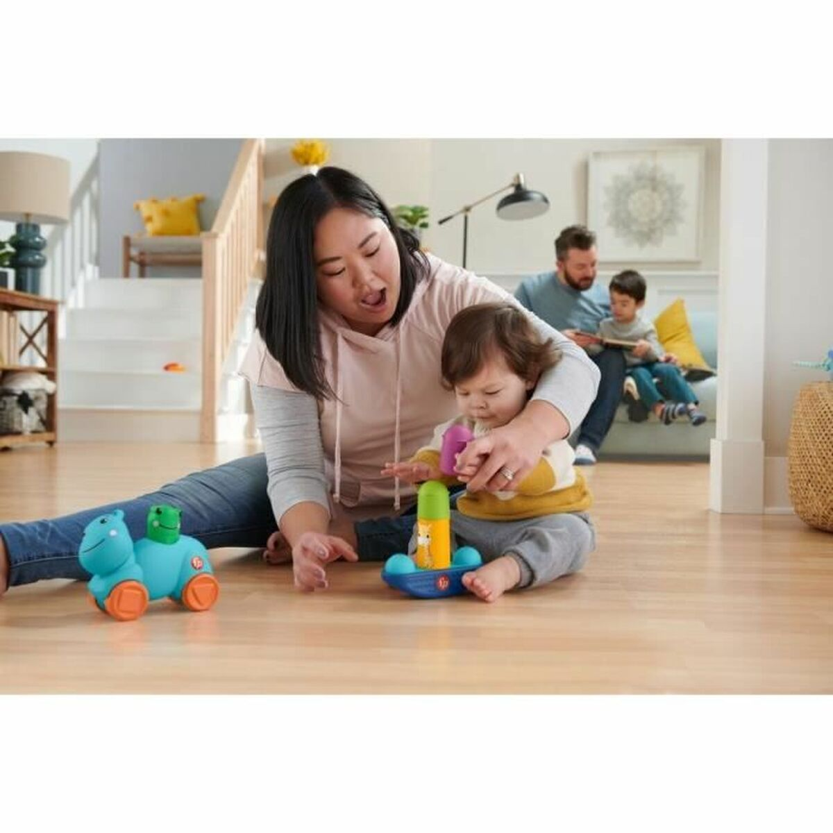 Eine Mutter und ein Baby spielen mit Spielzeug. Ein Mann und ein Junge sitzen im Hintergrund.