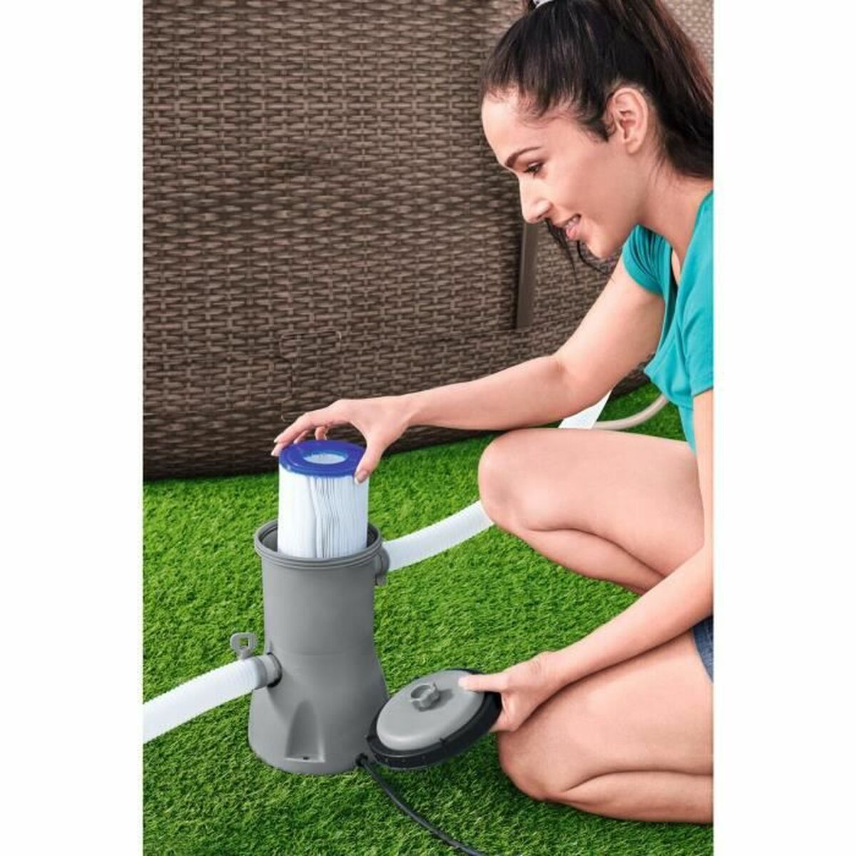 Vrouw bij zwembadfilter. Ze houdt een wit filter vast, groen gras.