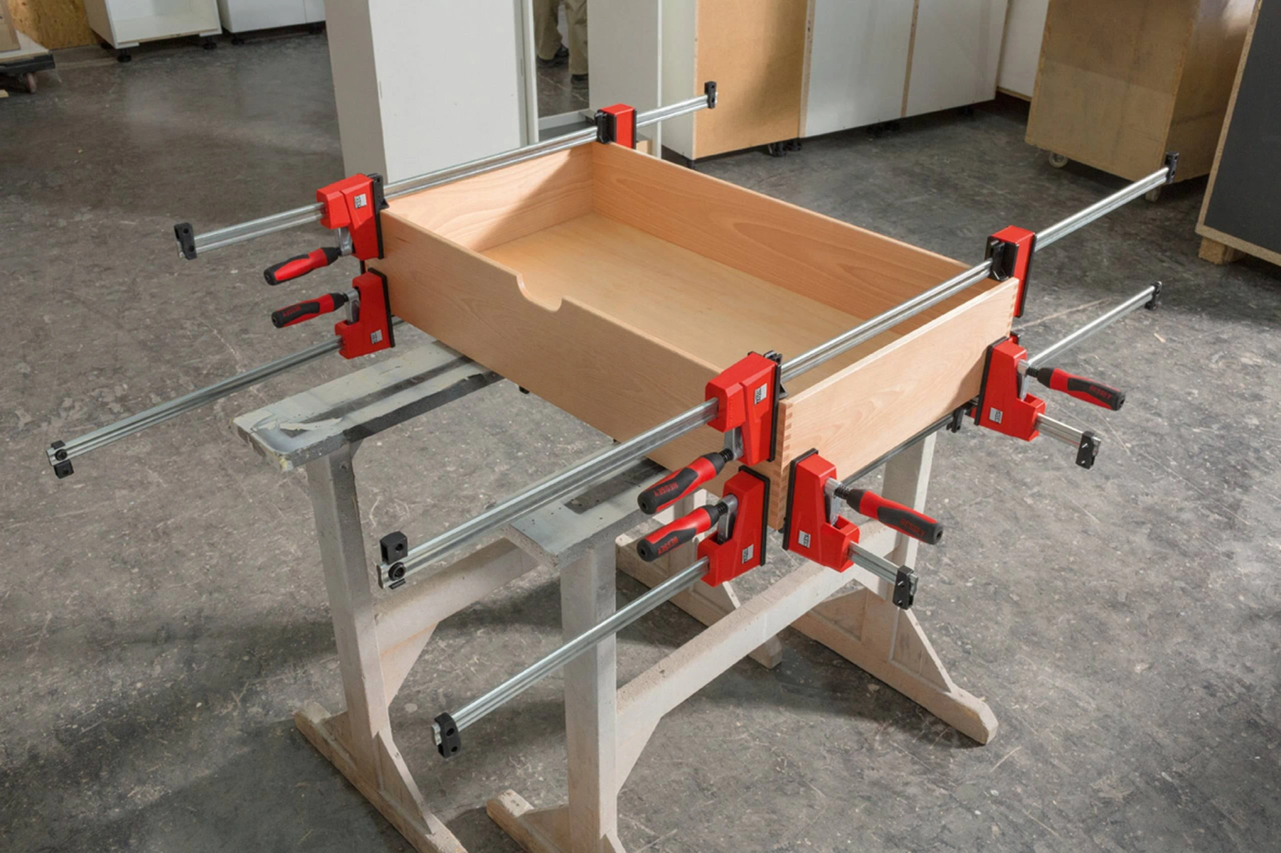 Un cajón de madera en proceso de montaje con abrazaderas. Abrazaderas rojas son visibles.
