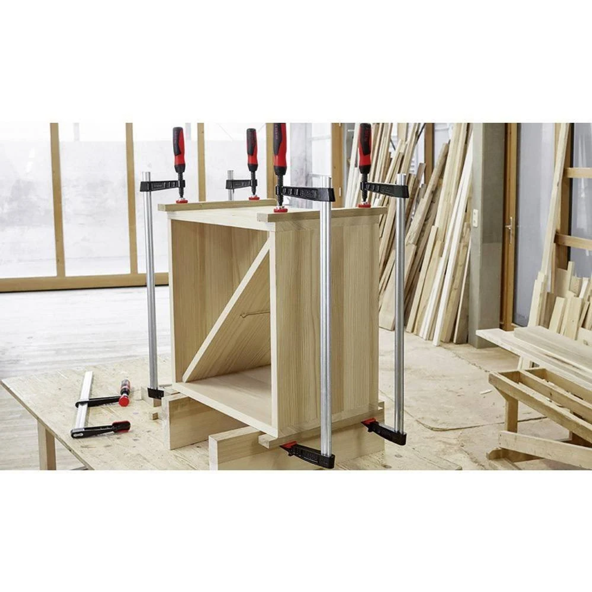Wooden cabinet being assembled with clamps. Saw and screws are on the table.