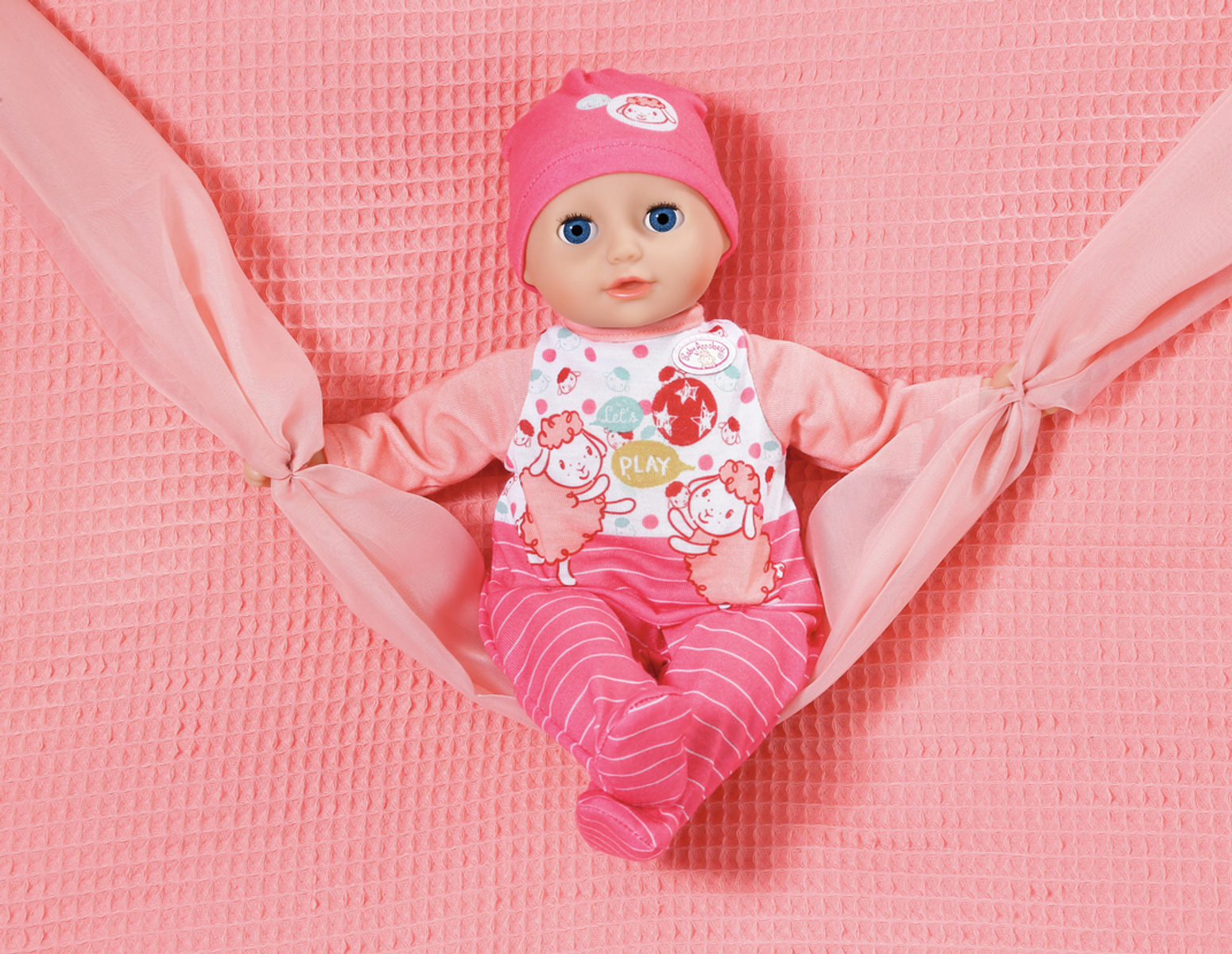 Babypuppe in rosa Kleidung, liegend auf einer rosafarbenen Decke mit rosa Schal.