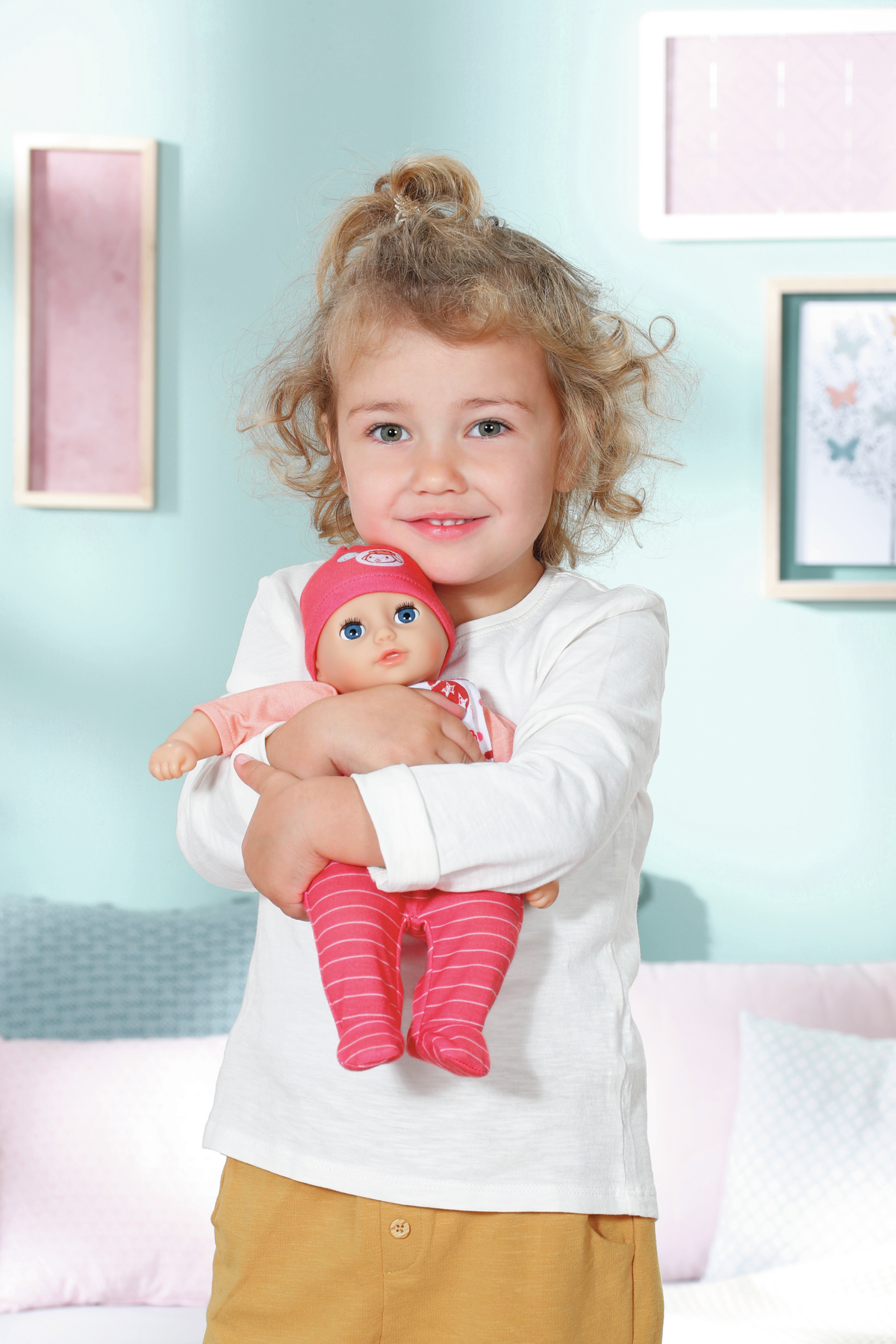 Ein junges Mädchen hält eine Babypuppe. Sie trägt ein weißes Hemd und einen rosa Hut.