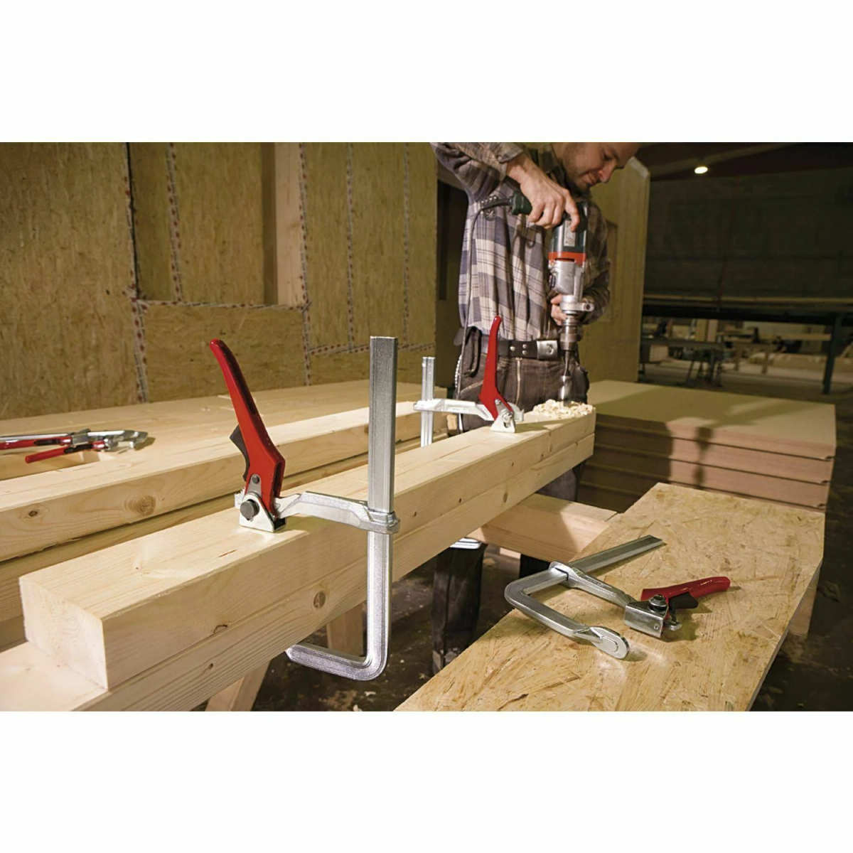 Un hombre taladrando un agujero en una viga de madera, con abrazaderas sujetando la viga.