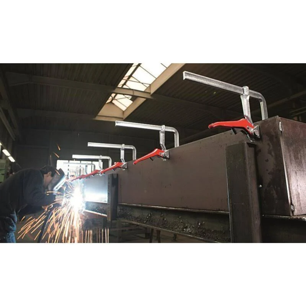 Soldador trabajando con metal. Las abrazaderas sujetan las piezas de metal. Son visibles chispas y luz.