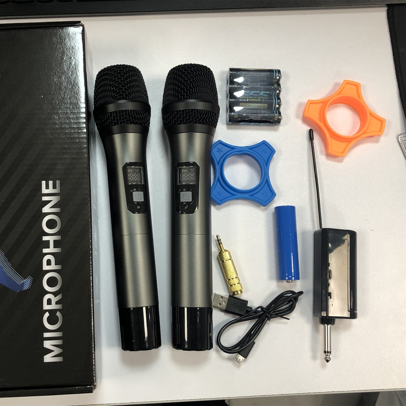 Dwa mikrofony, baterie i akcesoria na białej powierzchni.