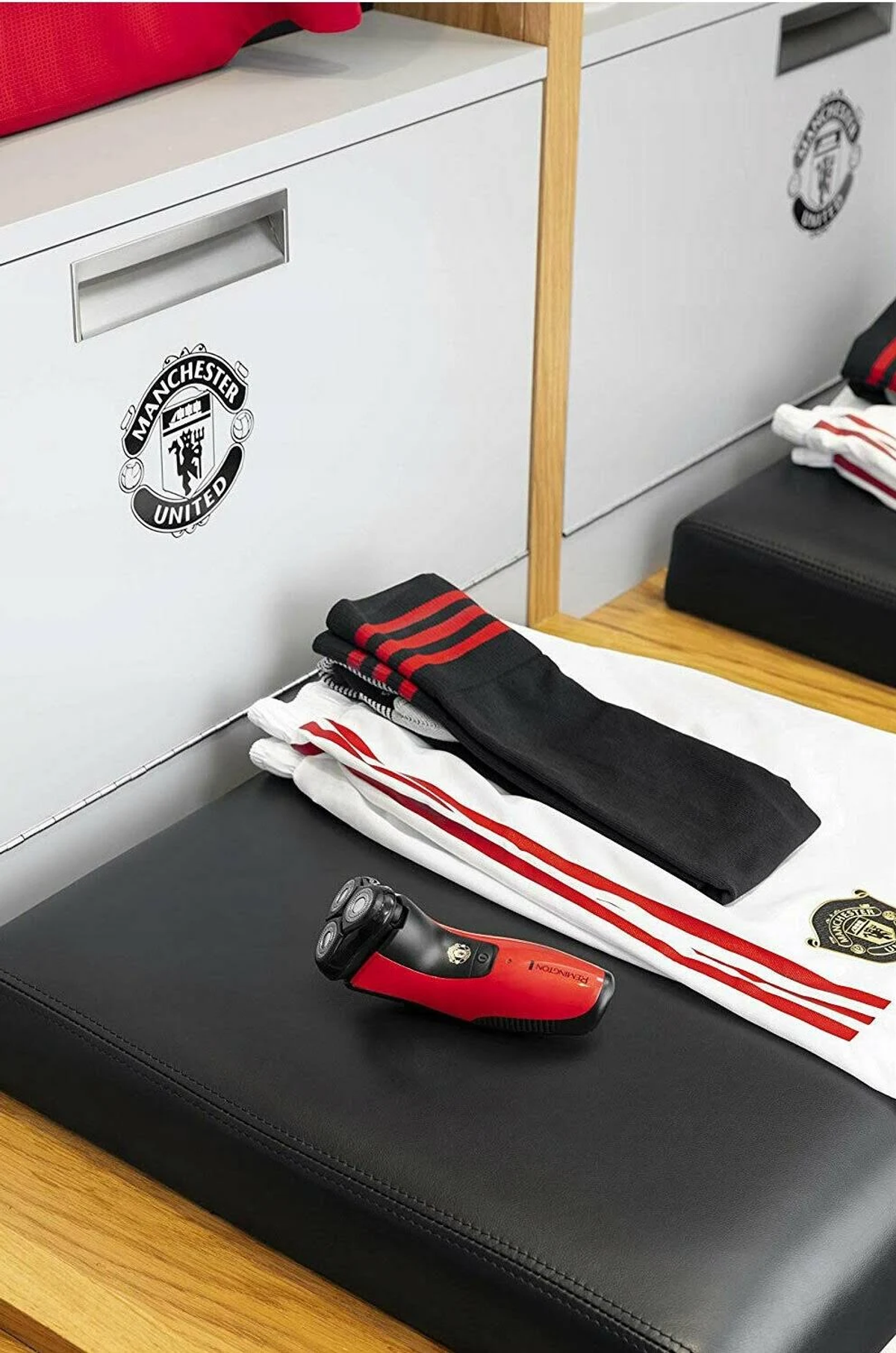 Escena del vestuario del Manchester United. Calcetines negros con rayas rojas, maquinilla y camiseta en banco.