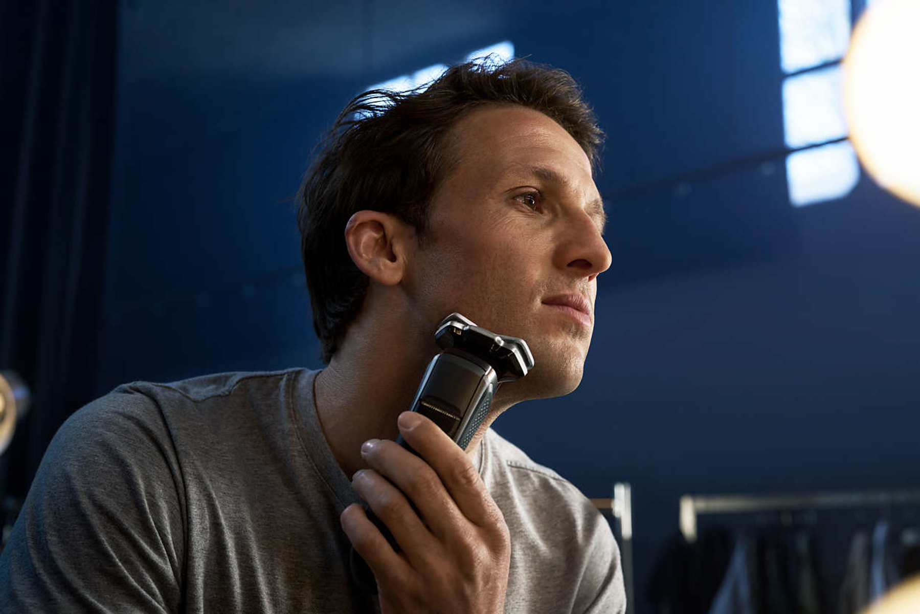 Mężczyzna goli twarz golarką elektryczną, patrząc w lustro.