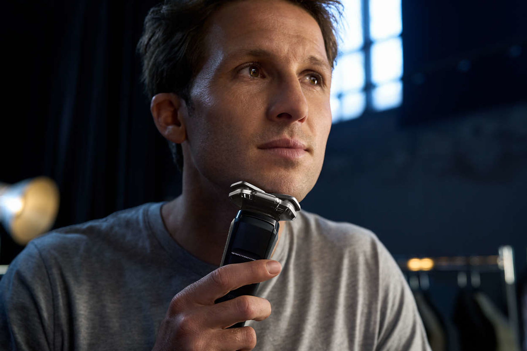 Mężczyzna goli się czarno-srebrną golarką Philips, patrząc w górę. Rozmyte tło.