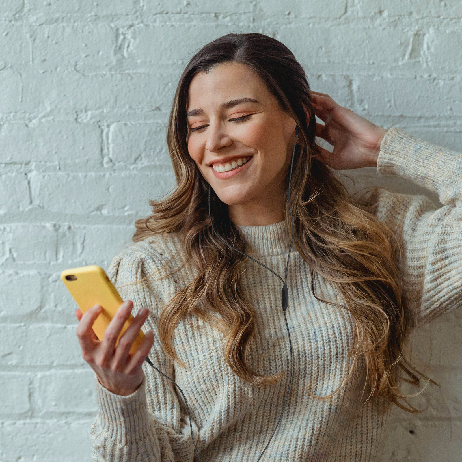Una donna sorridente con lunghi capelli castani che ascolta musica sul suo telefono con le cuffie.