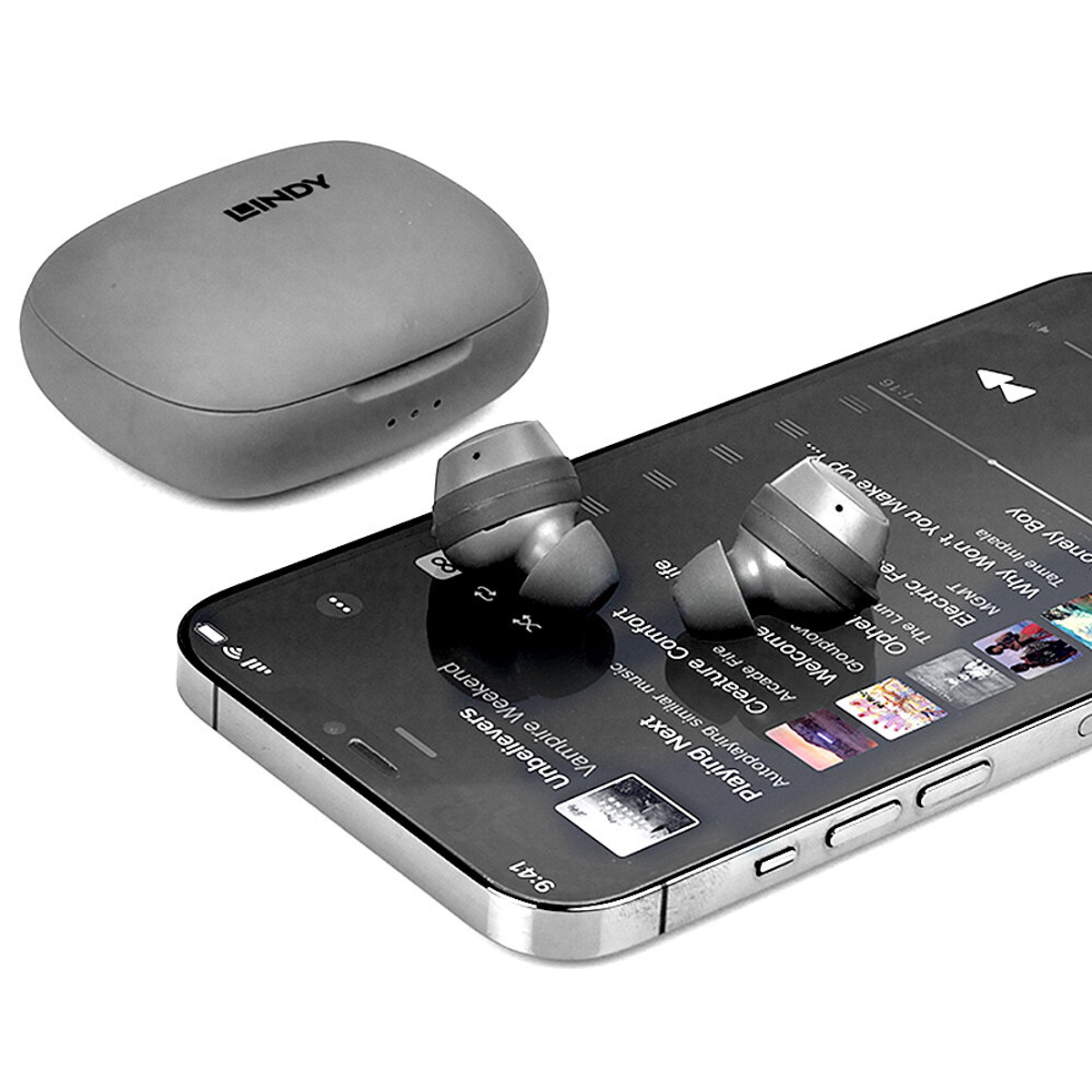 Graue Ohrhörer und ein Ladecase befinden sich in der Nähe eines Smartphones. Das Telefon zeigt Musik.
