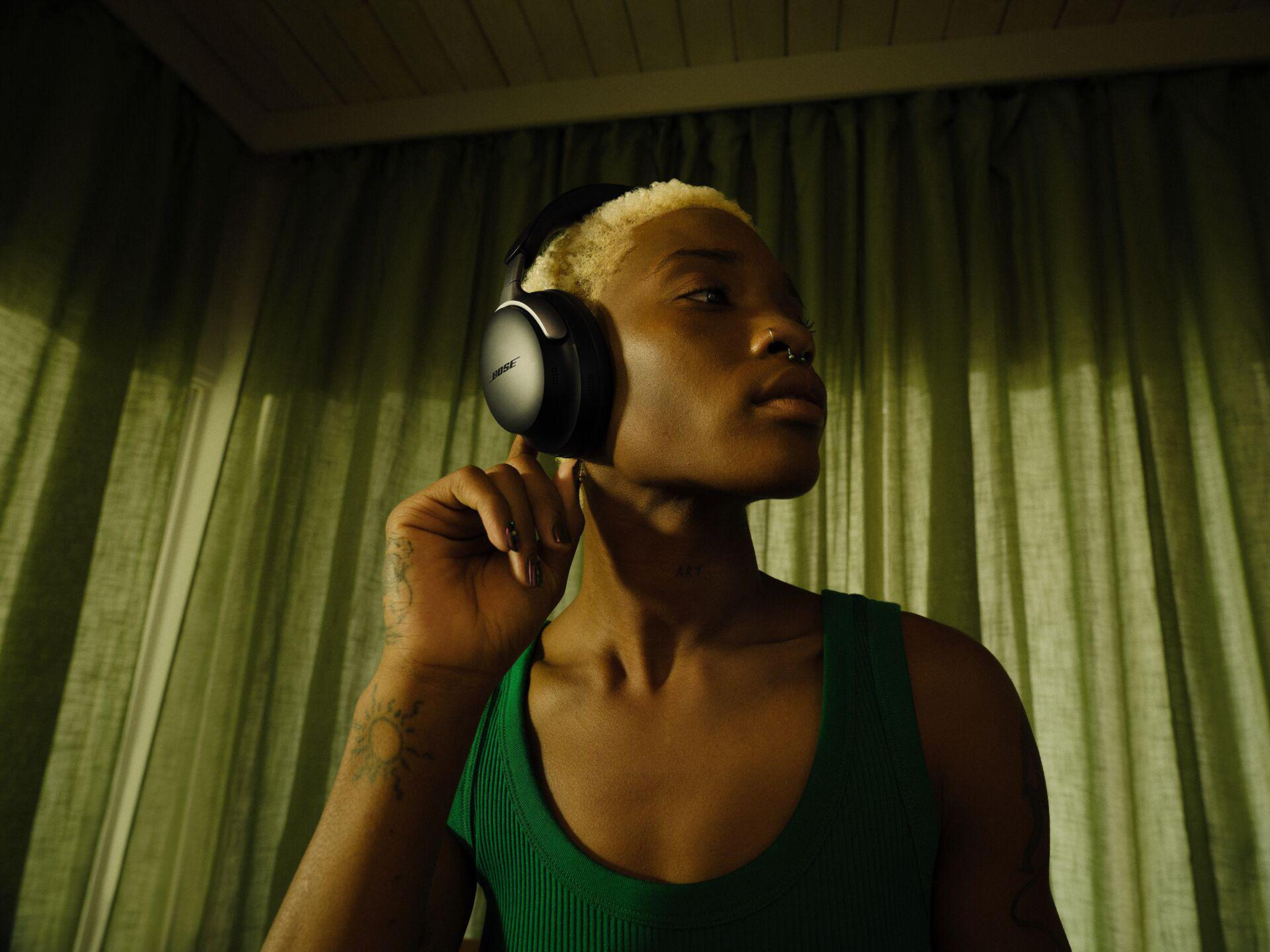 Osoba w czarnych słuchawkach, zielonym podkoszulku, w pomieszczeniu z zielonymi zasłonami.