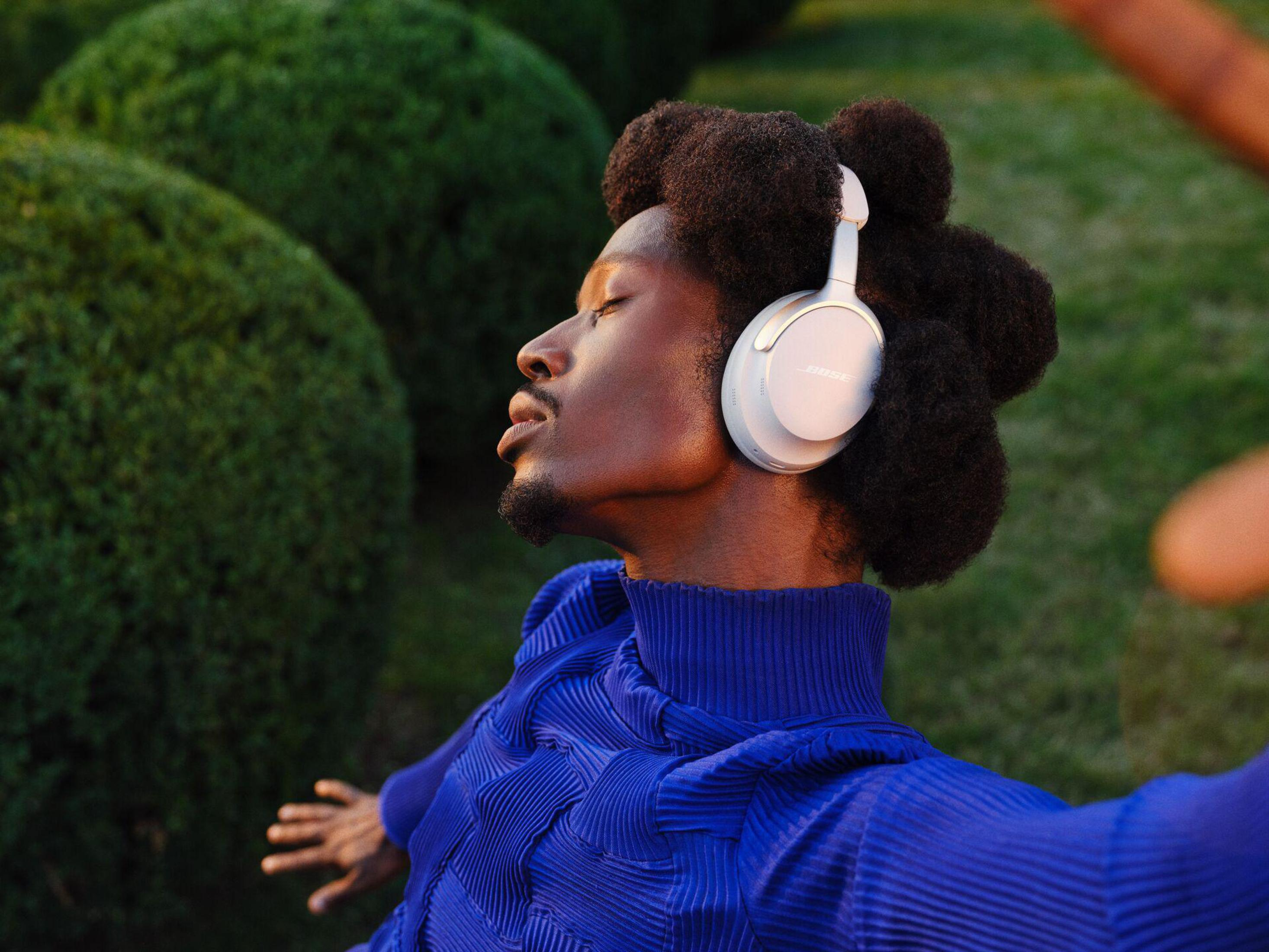 Mężczyzna ze słuchawkami w ogrodzie, niebieska koszula, zamknięte oczy.