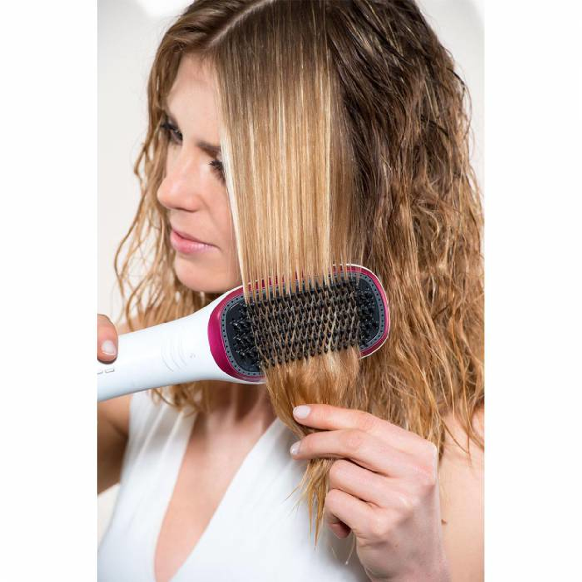 Una mujer usa un cepillo para peinar el cabello. El cepillo es blanco y rosa.