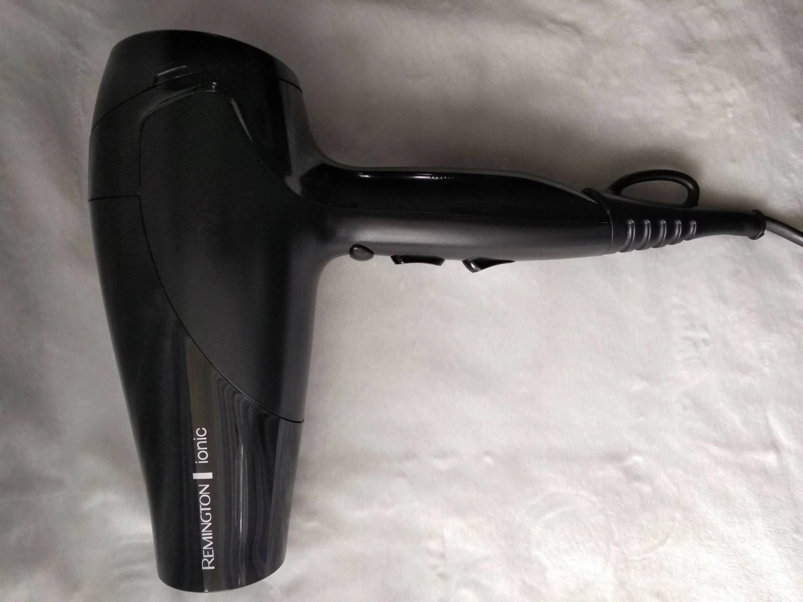 Asciugacapelli nero su un lenzuolo bianco. Il marchio Remington è visibile. Sfondo bianco.