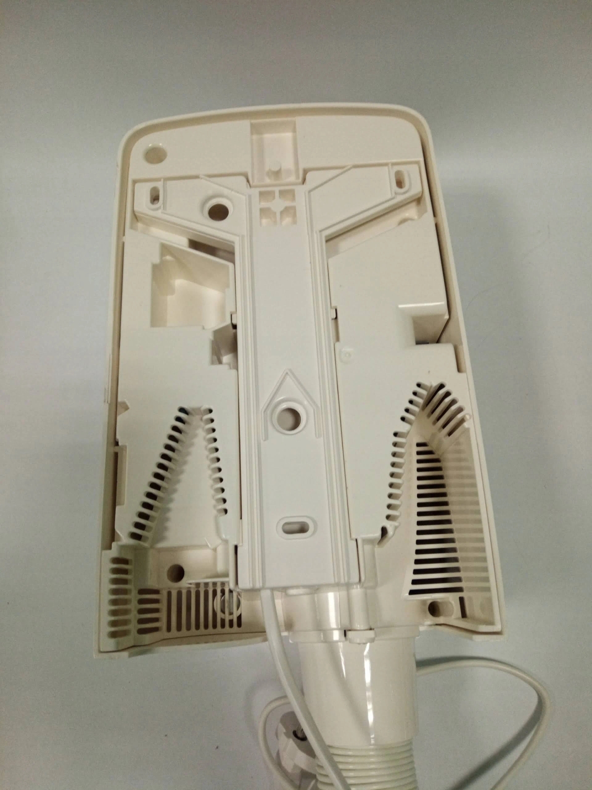 Widok wewnętrzny białej suszarki do włosów, ze szczegółami wentylacji i przewodem, na białym tle.