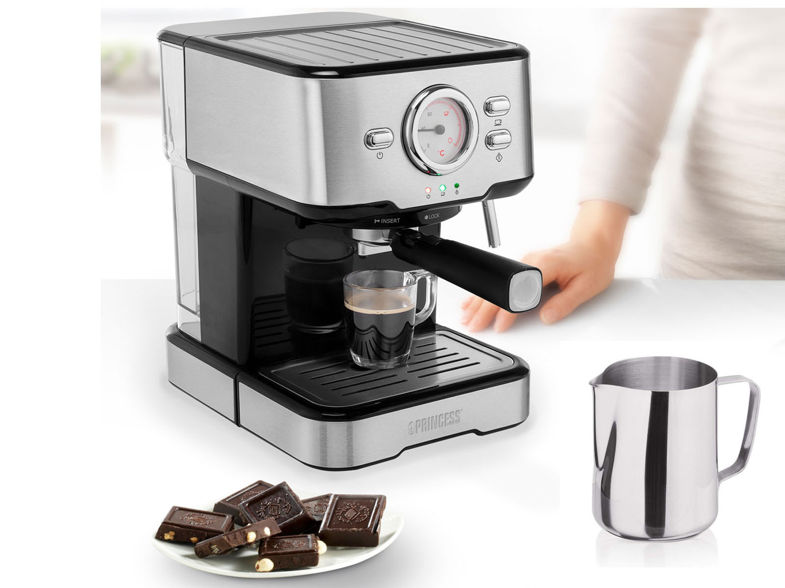 Eine Espressomaschine mit einem Glas Kaffee, einem Teller Schokolade und einem Milchkanne.