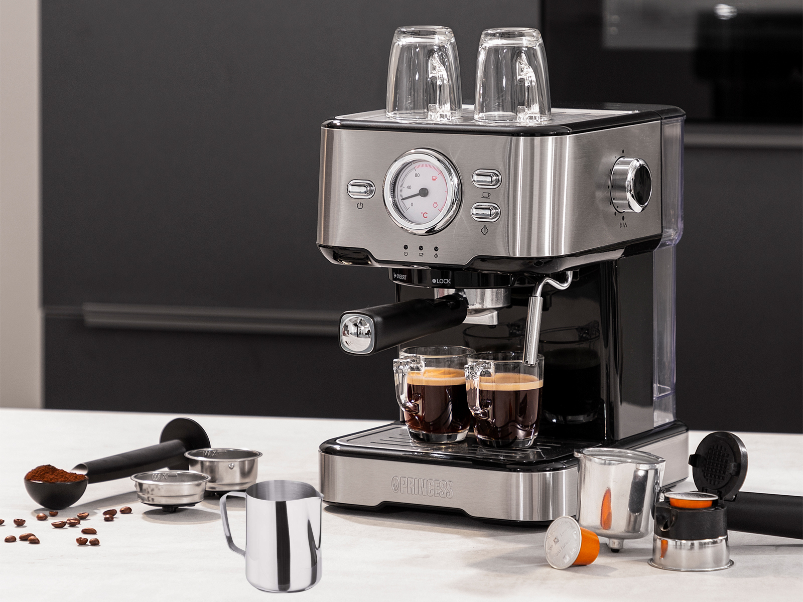 Espressomaschine mit zwei Kaffeetassen, zwei Gläsern und Zubehör auf Marmoroberfläche.