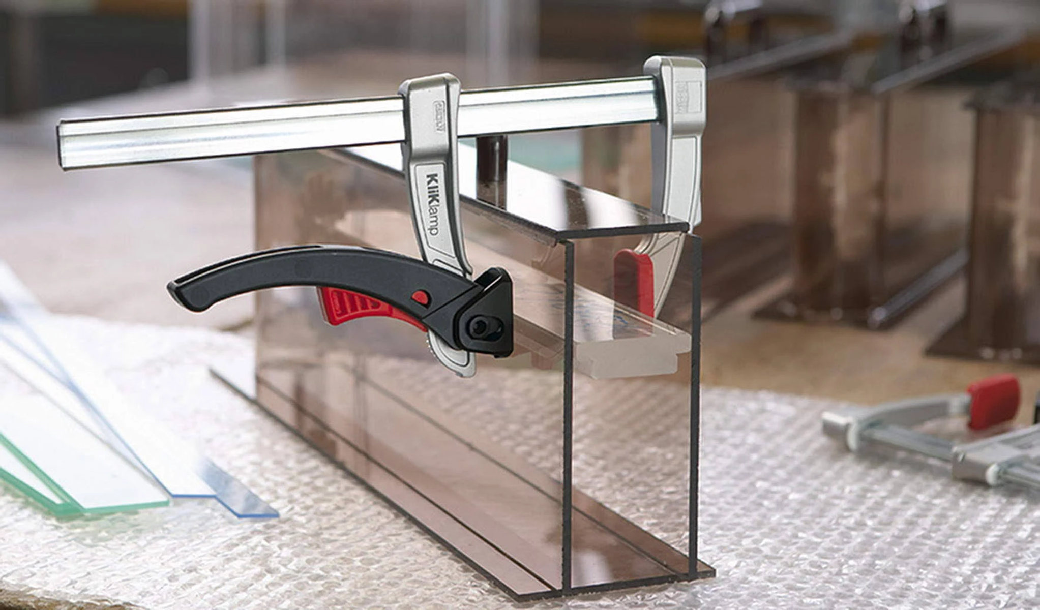 Dos abrazaderas sujetan una forma rectangular transparente, con otras láminas de vidrio cerca.