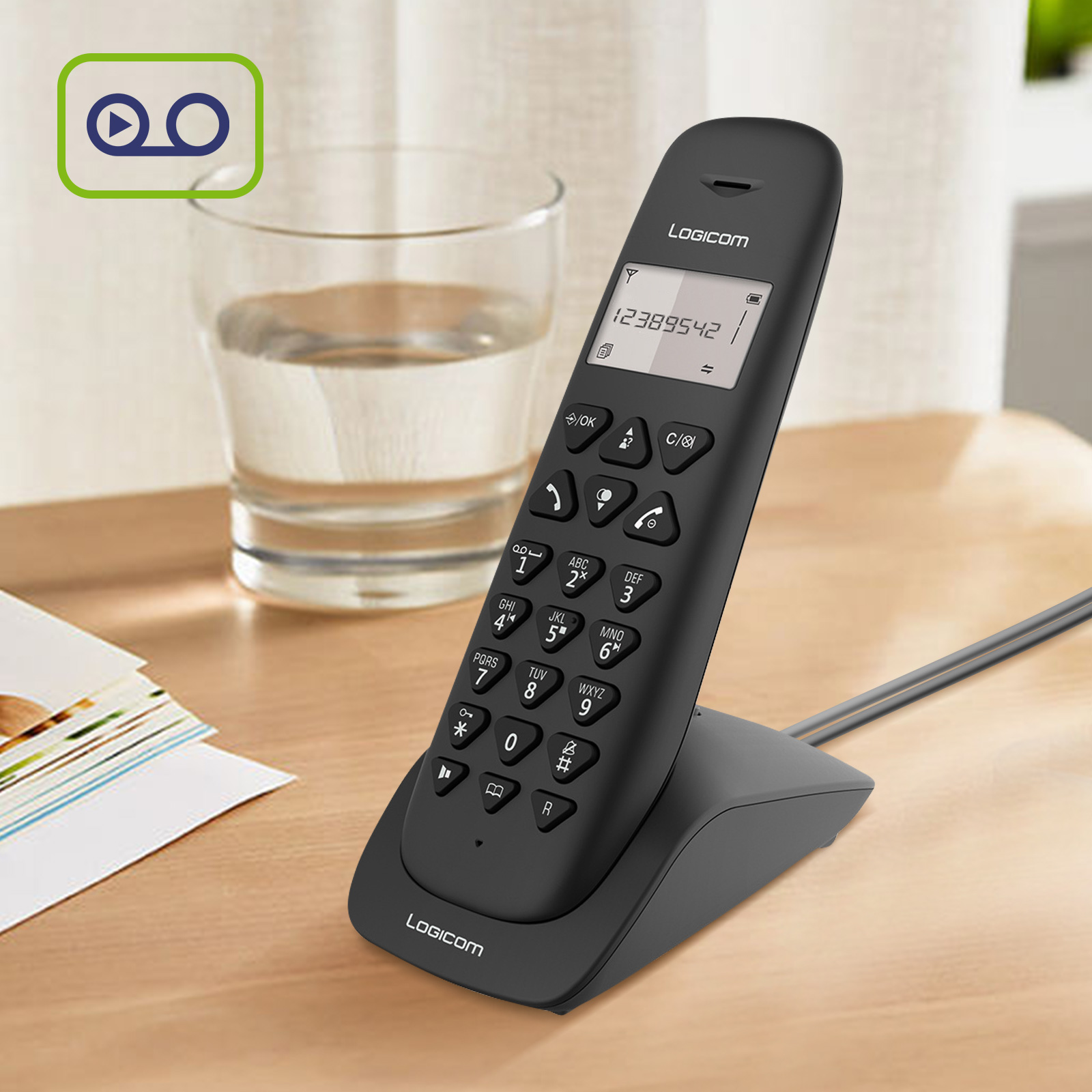 Telefono cordless nero su un tavolo con un bicchiere e un blocco note.