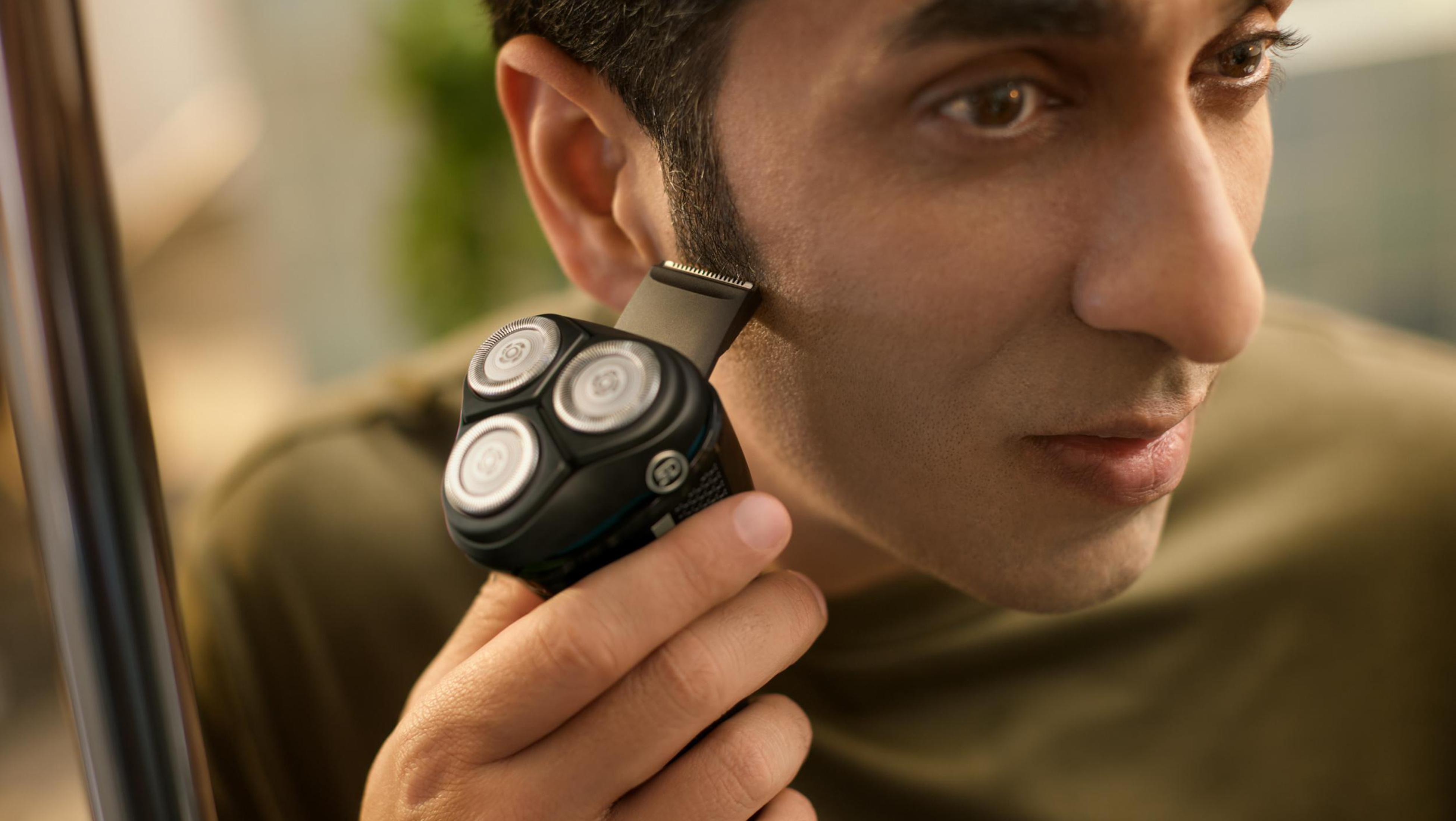 Mężczyzna goli twarz czarną golarką elektryczną.