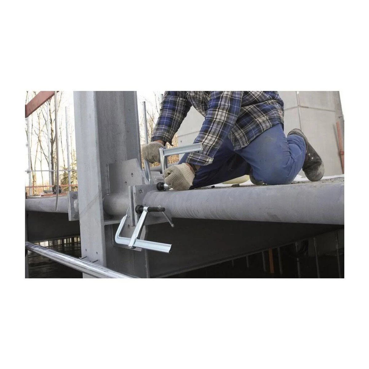Eine Person arbeitet an einer Metallkonstruktion und verwendet ein Werkzeug. Die Struktur ist silber und grau.