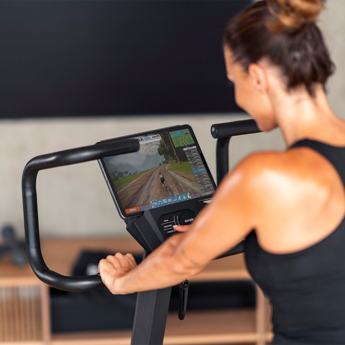 Frau auf einem Fahrradtrainer, die einen Bildschirm mit einer Radfahrsimulation betrachtet.