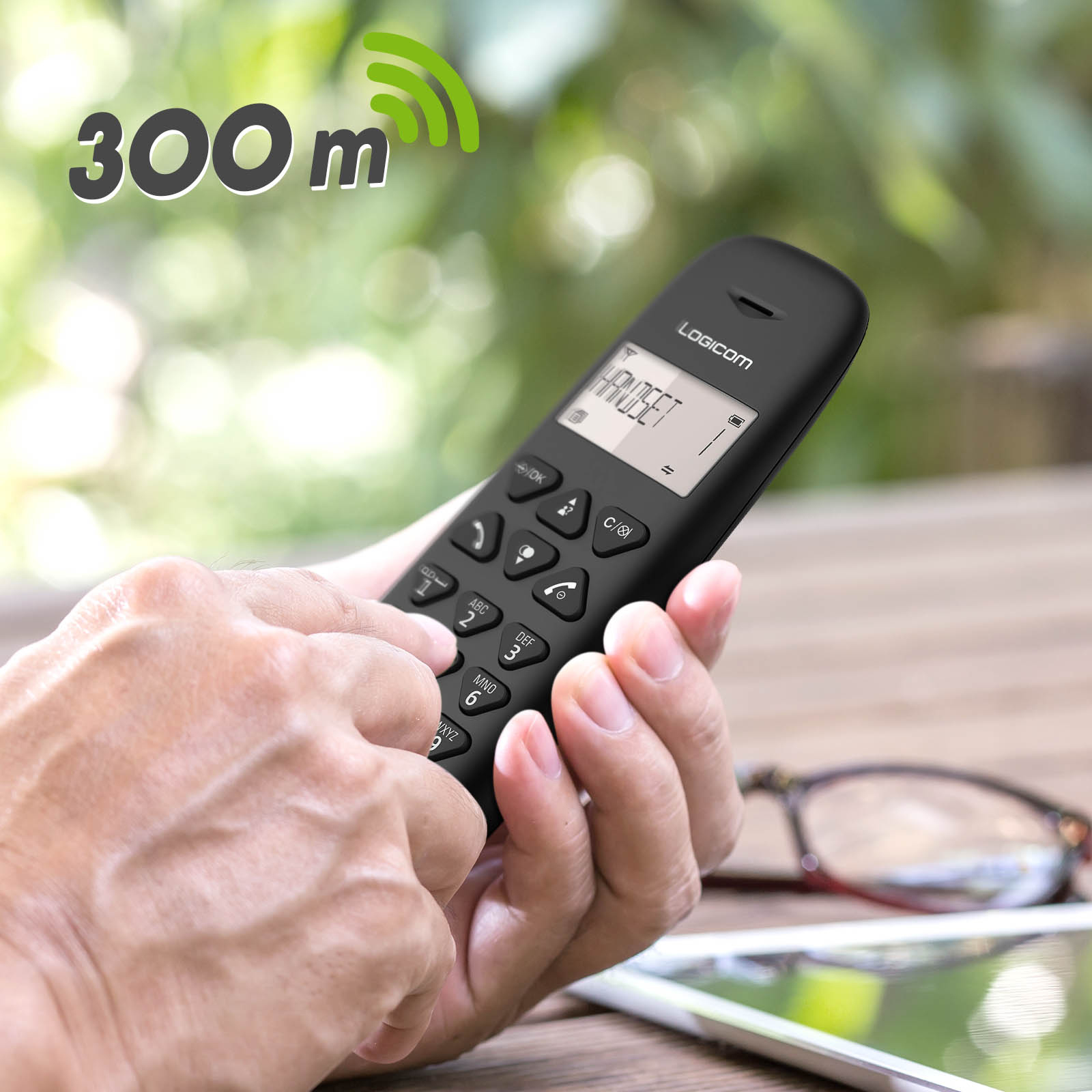 Un telefono cordless nero tenuto da una mano, con uno sfondo sfocato.