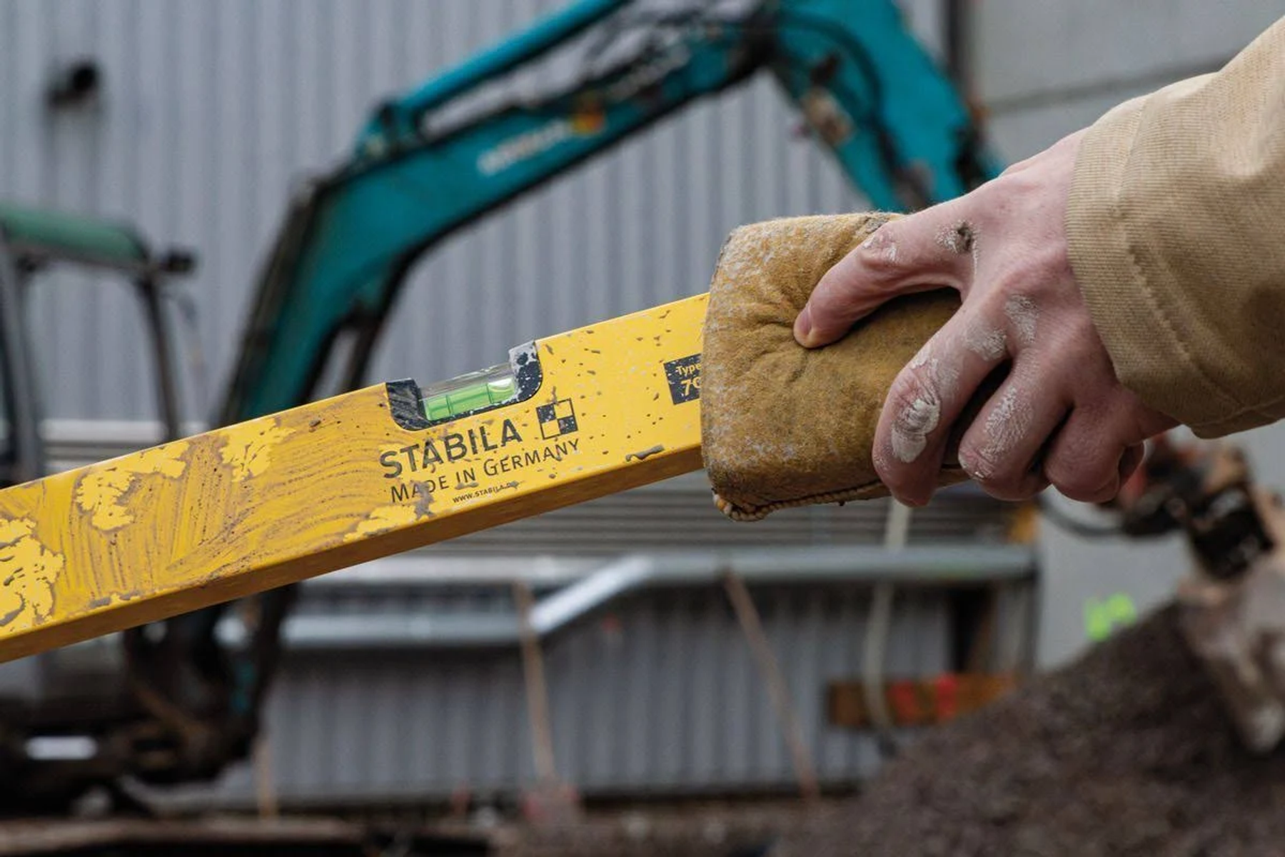 Hand hält Wasserwaage. Gelbe Wasserwaage mit der Aufschrift STABILA, Hintergrund Baustelle.
