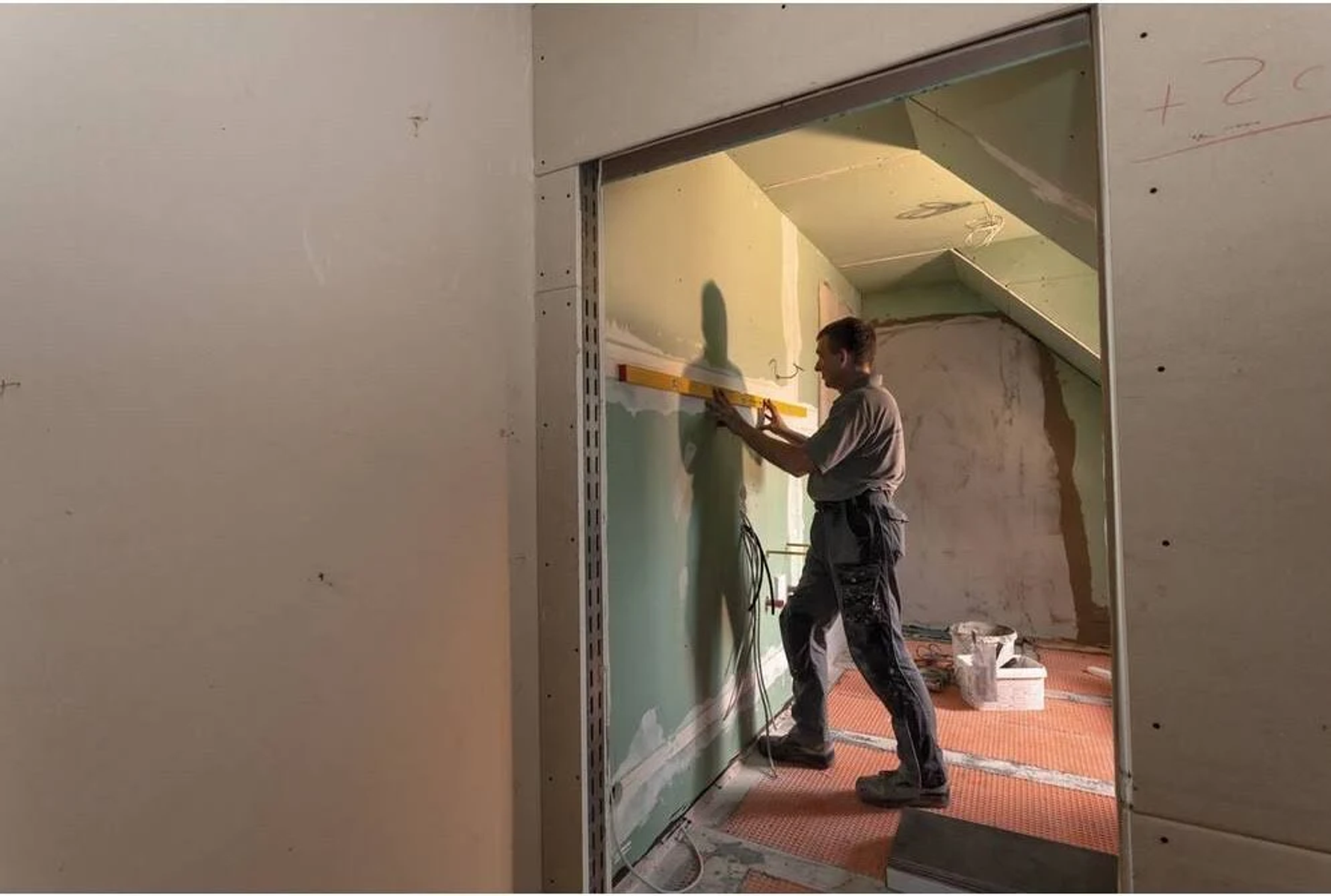Ein Mann nivelliert im Bau mit einer Wasserwaage eine Wand.