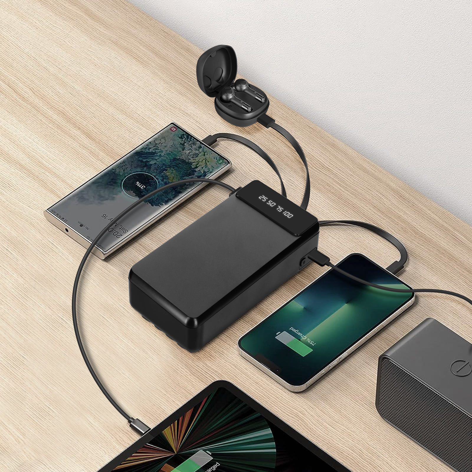 Batterie externe noire chargeant téléphones et écouteurs sur une table en bois. Affiche les pourcentages.