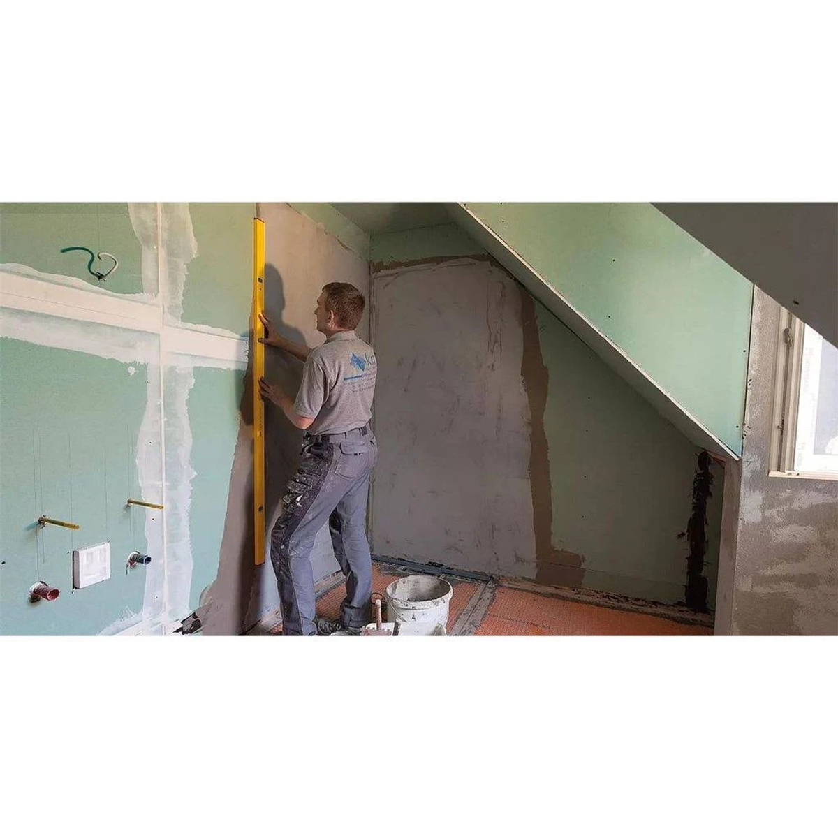 Mann benutzt Wasserwaage an einer Wand, Trockenbau und Eimer auf dem Boden.
