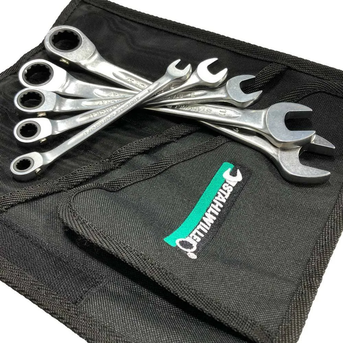 Satz Schraubenschlüssel auf schwarzem Stoff, mit grün-weißem Logo-Aufnäher.
