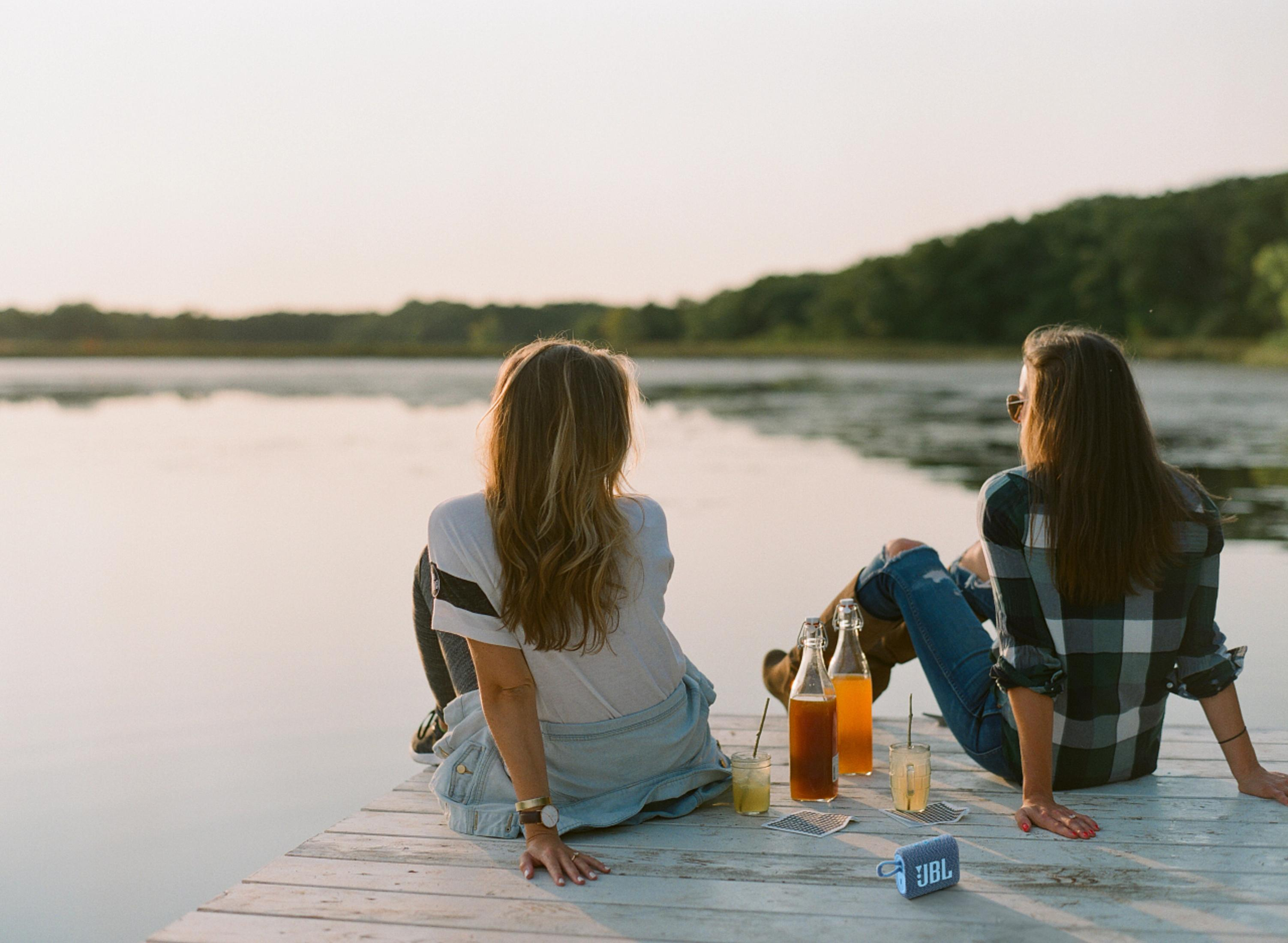 Deux femmes sur une jetée, face à l'eau, avec des boissons et un haut-parleur.
