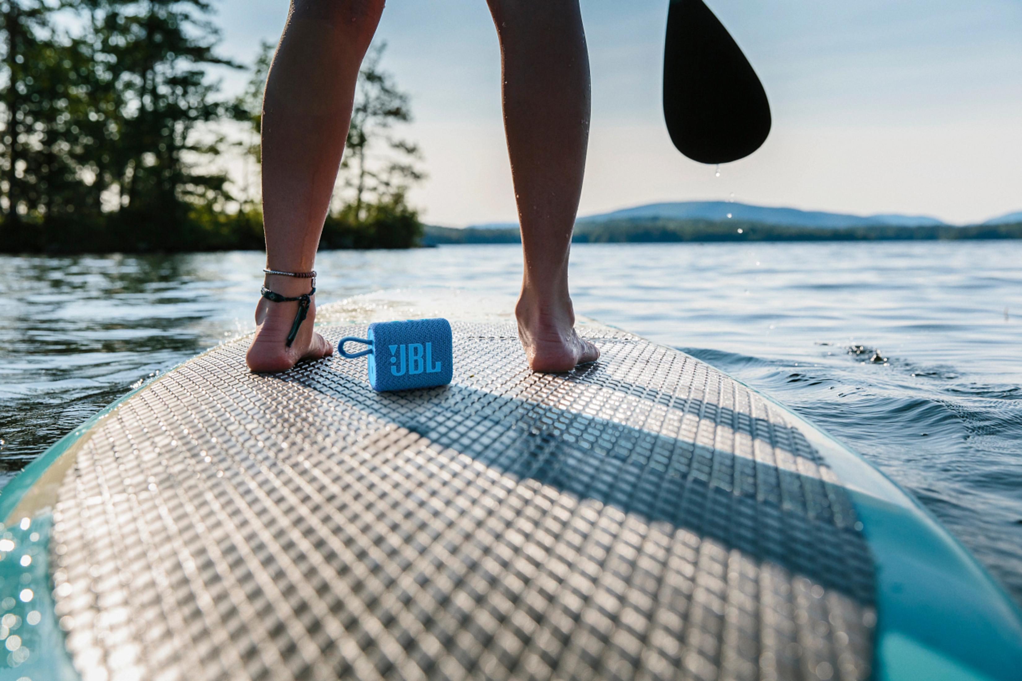 Pieds sur un paddleboard avec un haut-parleur bleu. Une pagaie est dans l'eau.