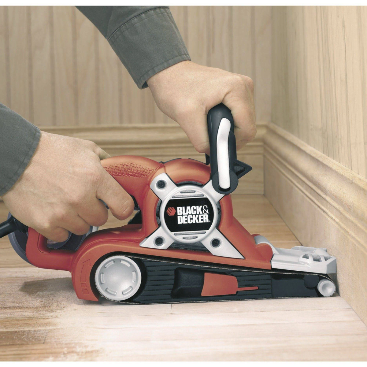 Eine Person benutzt einen Black & Decker Schleifer auf einer Holzfußleiste.