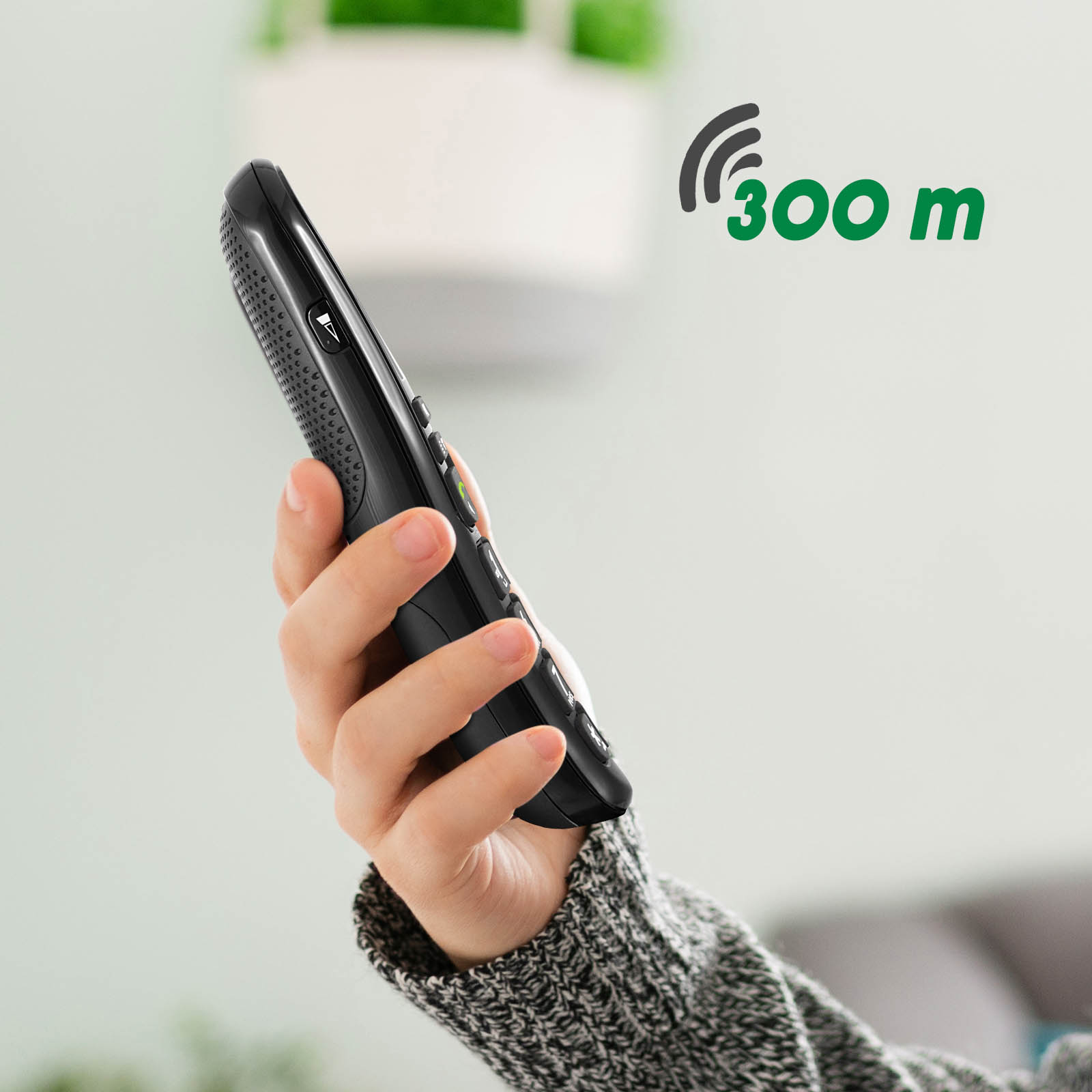 Una mano sosteniendo un teléfono inalámbrico negro. El texto verde muestra 300 m, indicando el alcance.