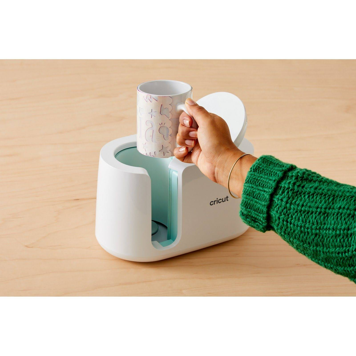 Eine Hand hält einen bedruckten Becher in einer weißen Cricut-Becherpressmaschine.